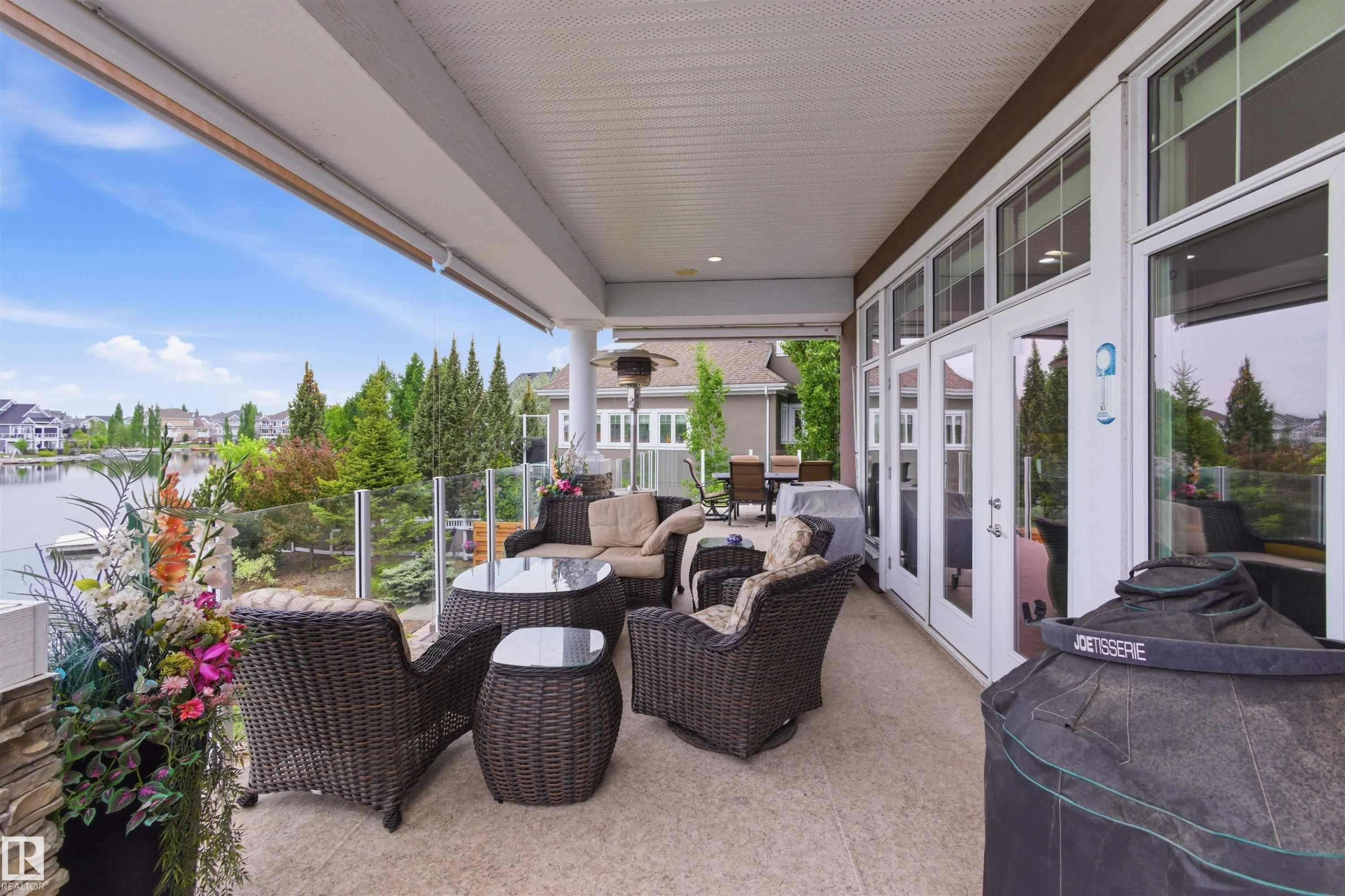 Covered outdoor patio featuring a textured concrete surface, glass railing, and water frontage - 9003 16 Avenue Sw, Edmonton, AB - Outdoor With Deck Patio Veranda With Exterior