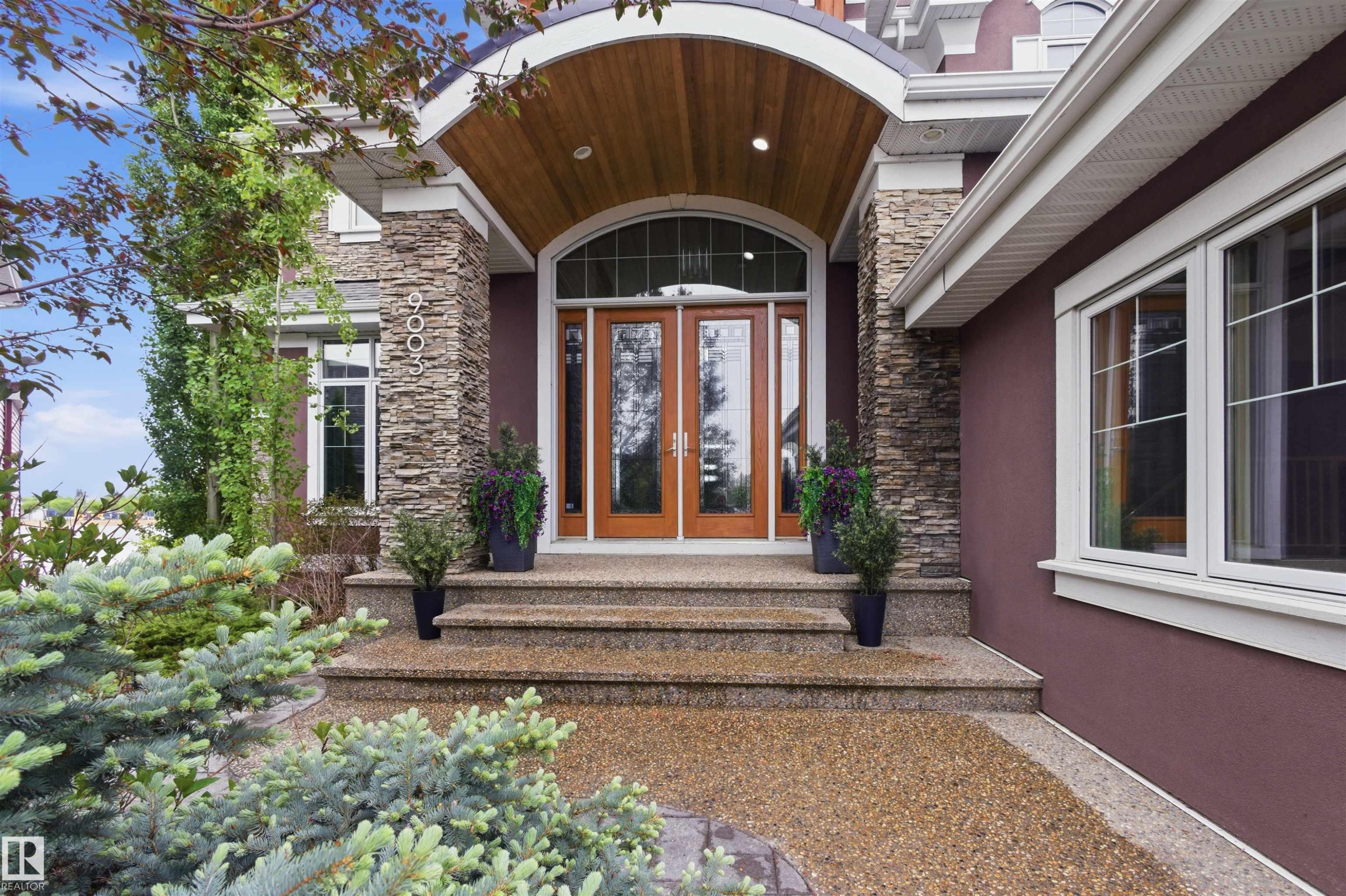 Grand arched entry with wood-paneled ceiling, double wood doors with glass inserts, stacked stone columns, and complementary stucco siding - 9003 16 Avenue Sw, Edmonton, AB - Outdoor