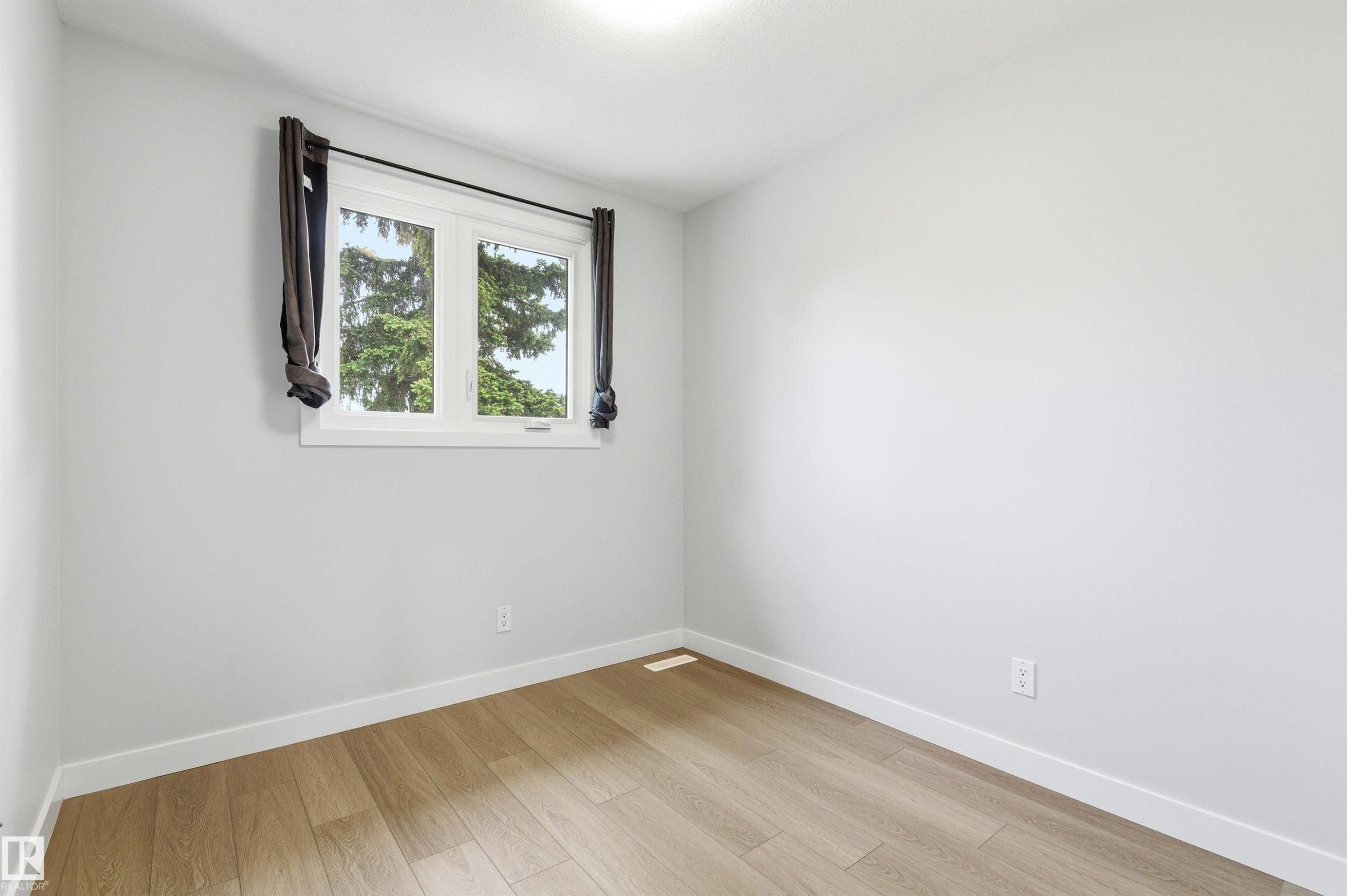 Light-filled room featuring wood-finish flooring, white baseboards, and a white-framed window - 18353 66 Avenue, Edmonton, AB
