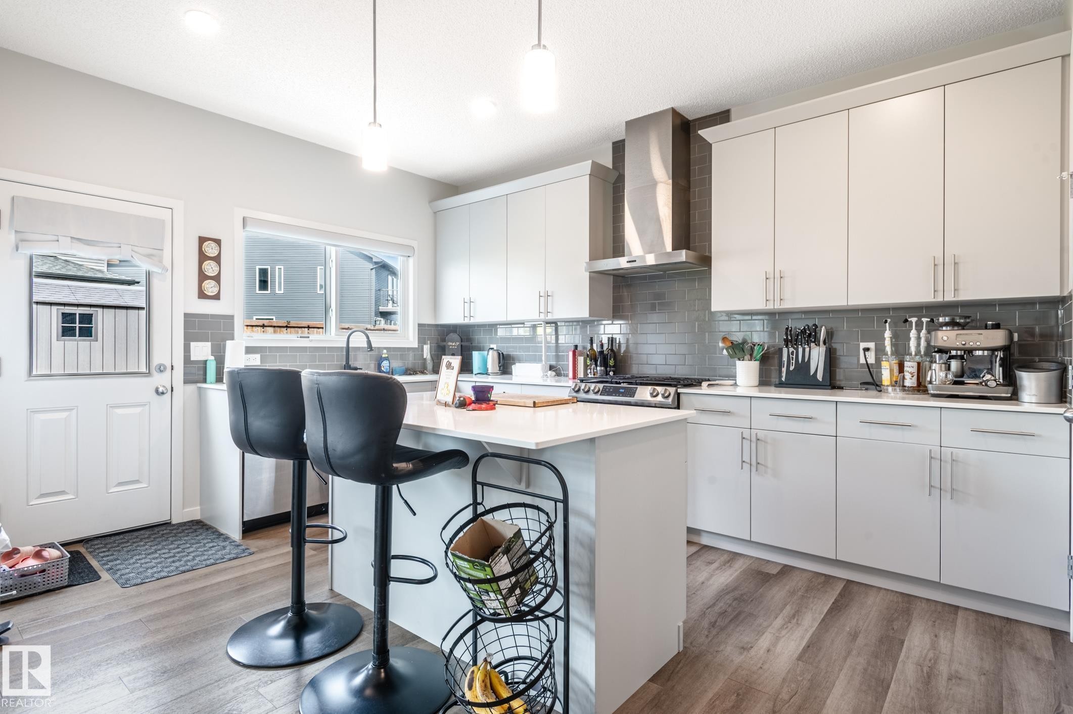 Modern kitchen featuring light gray cabinetry, stainless steel appliances, a subway tile backsplash, a central island with a white countertop, and wood-finish flooring - 17562 63A Street, Edmonton, AB