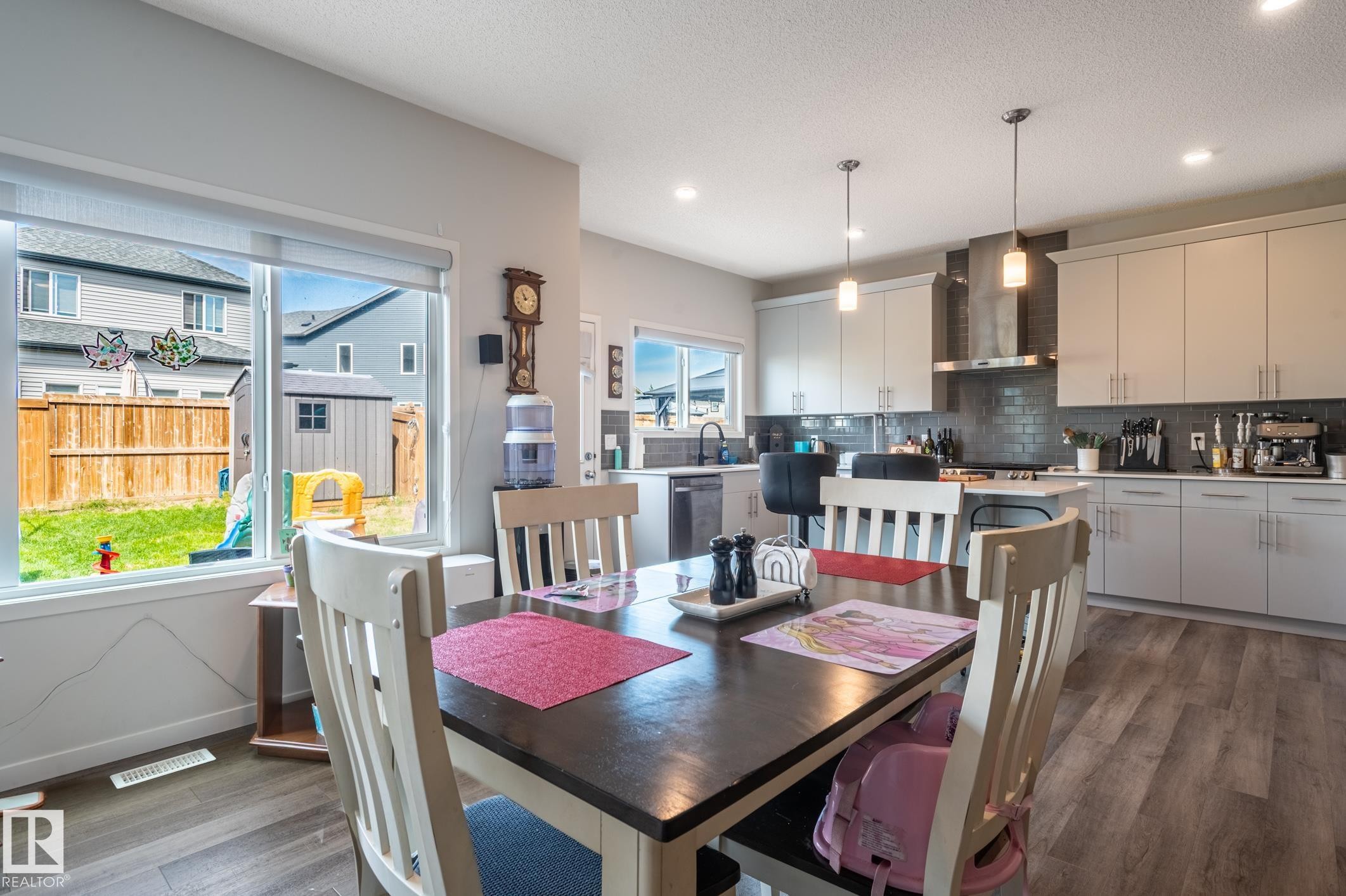 Open-concept kitchen and dining area featuring light wood-finish flooring, a kitchen island with seating, pendant lighting, and recessed ceiling lights - 17562 63A Street, Edmonton, AB