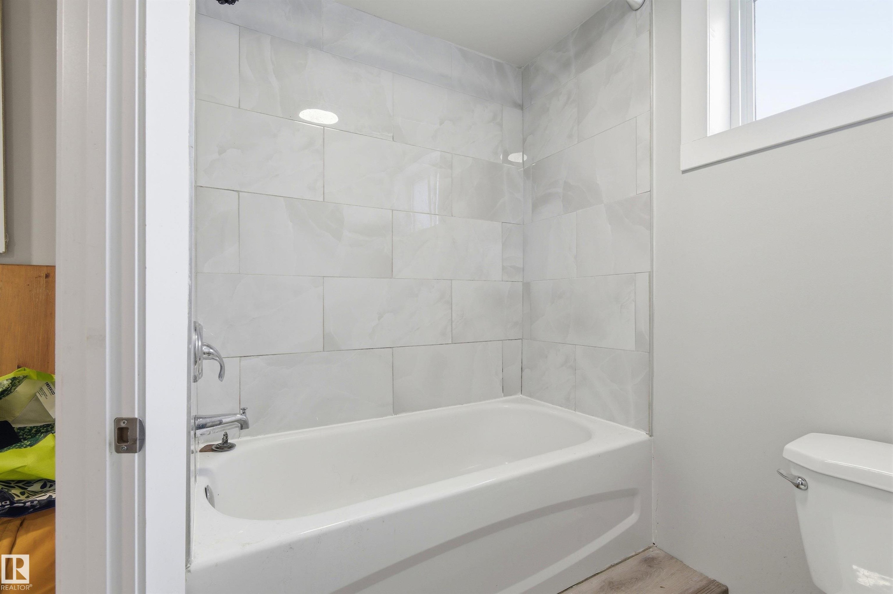 Bathtub with white subway tile surround, chrome fixtures, and a window for natural light - 7412/7414 83 Avenue Nw, Edmonton, AB - Indoor Photo Showing Bathroom