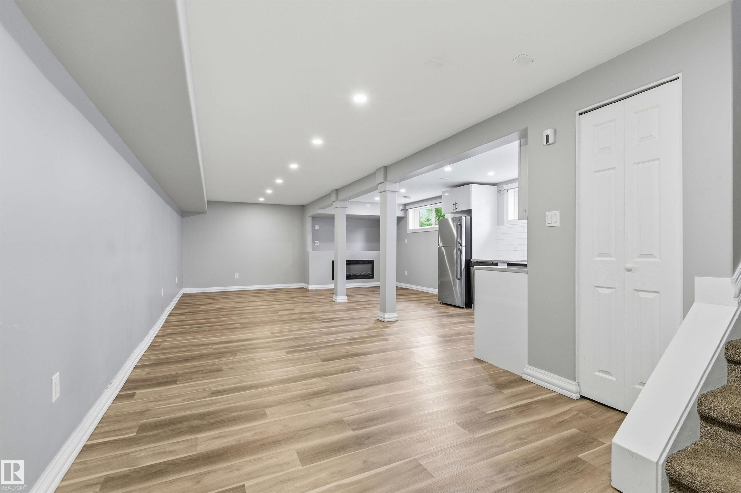 Spacious lower level featuring wood-finish flooring, recessed lighting, and a built-in fireplace - 7412/7414 83 Avenue Nw, Edmonton, AB - Indoor Photo Showing Other Room