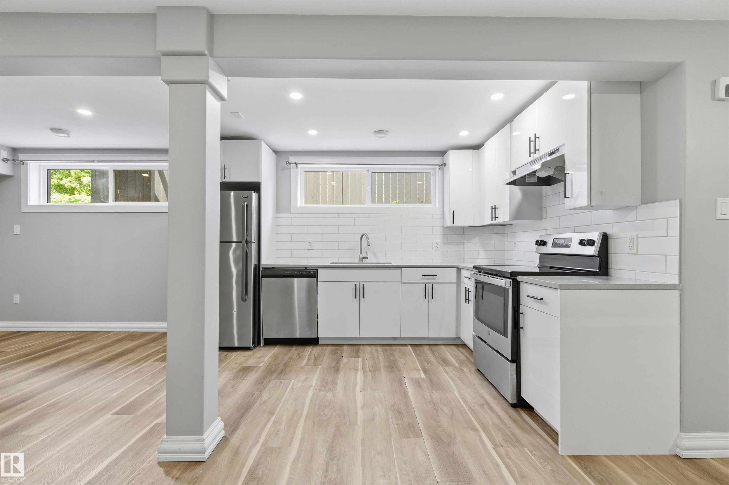 Open-concept kitchen featuring wood-finish flooring, white cabinetry, stainless steel appliances, a subway tile backsplash, and recessed lighting - 7412/7414 83 Avenue Nw, Edmonton, AB - Indoor Photo Showing Kitchen With Upgraded Kitchen
