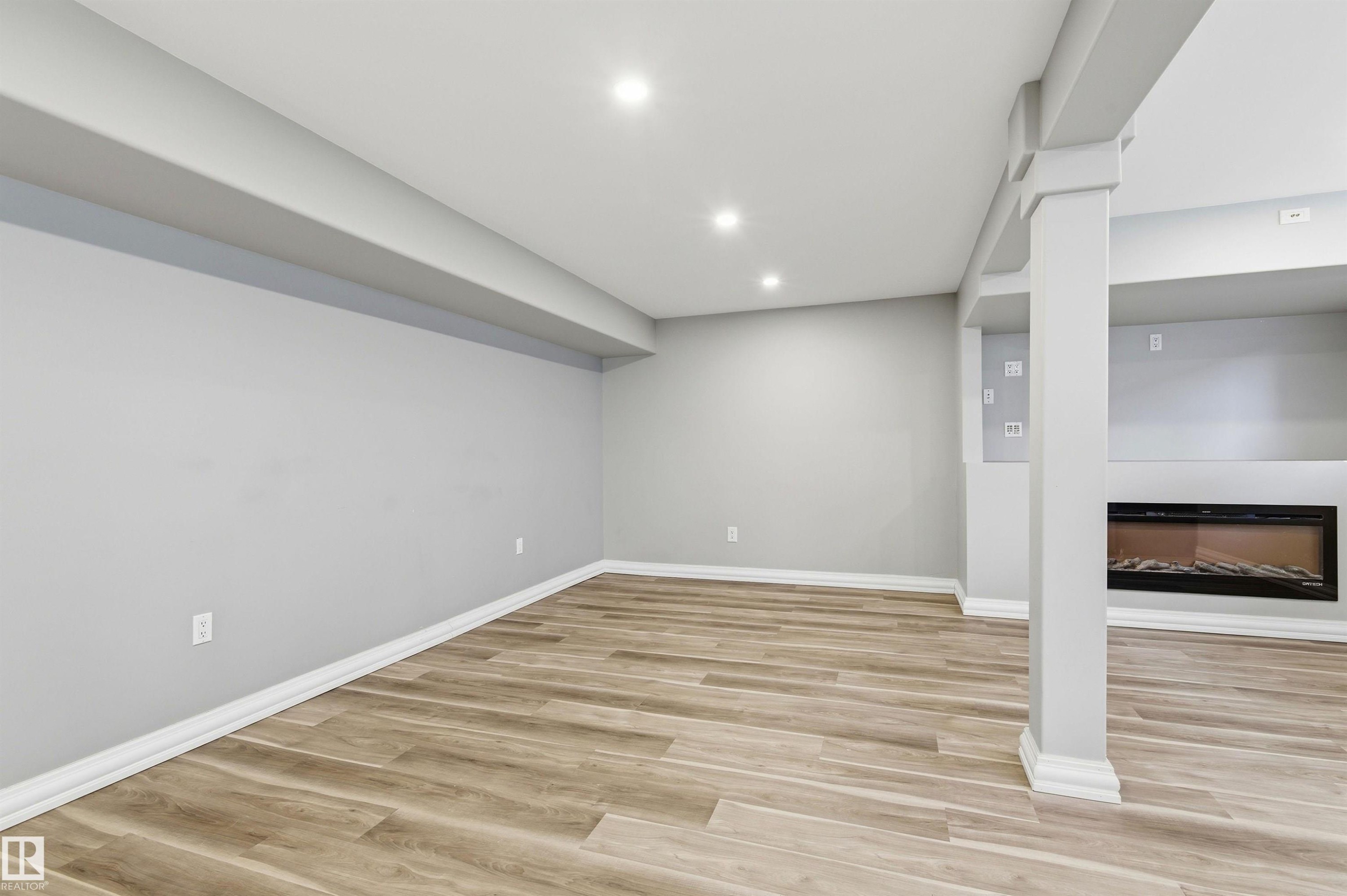 Spacious room featuring wood-finish flooring, recessed lighting, and a built-in linear fireplace - 7412/7414 83 Avenue Nw, Edmonton, AB - Indoor