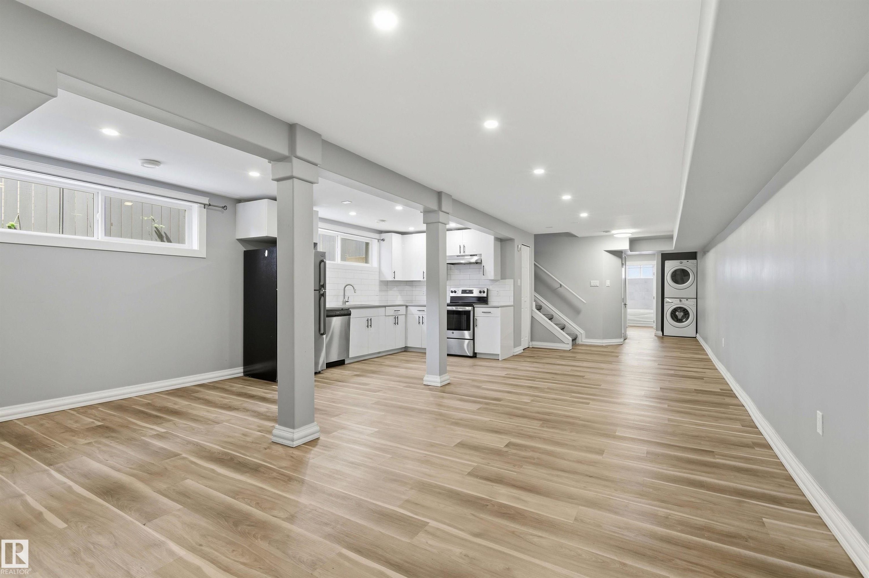 Open-concept living space featuring wood-finish flooring, recessed lighting, and a modern kitchen with white cabinetry and stainless steel appliances - 7412/7414 83 Avenue Nw, Edmonton, AB - Indoor Photo Showing Other Room