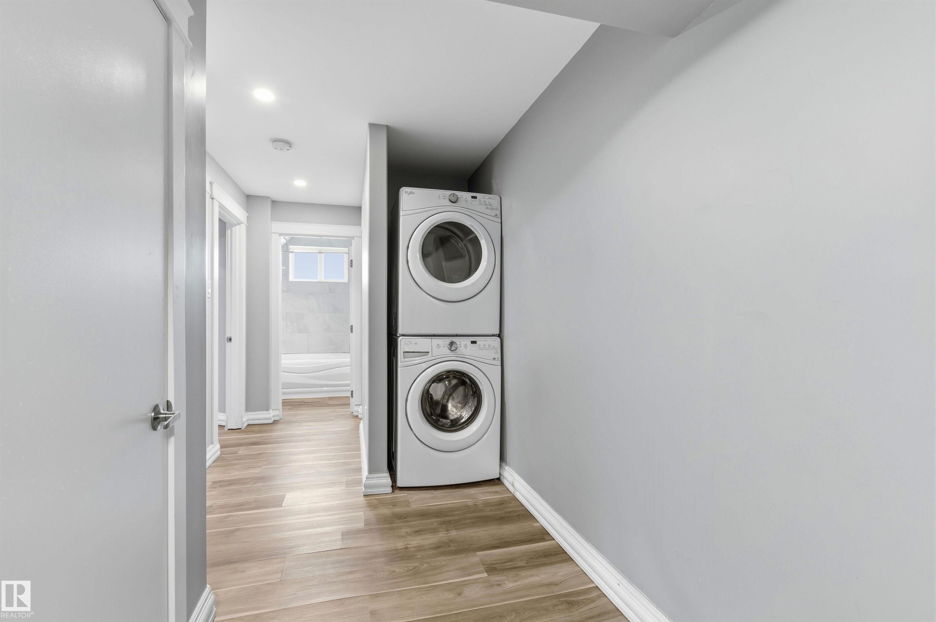 Hallway laundry alcove featuring a stacked white washer and dryer - 7412/7414 83 Avenue Nw, Edmonton, AB - Indoor Photo Showing Laundry Room