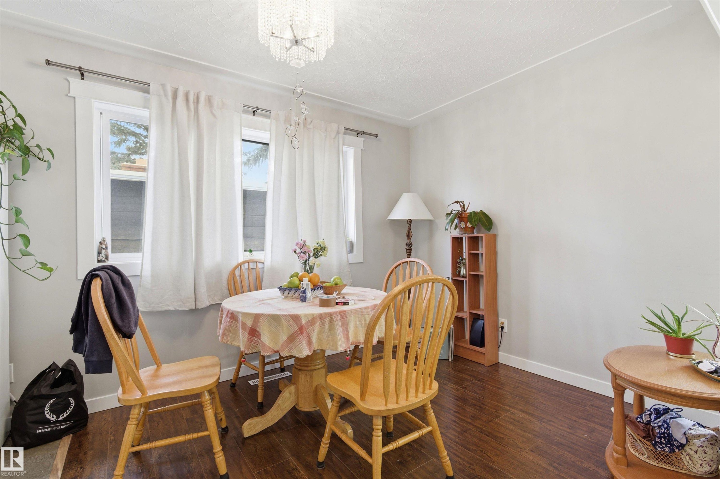 Dining area featuring wood-finish flooring, a crystal chandelier, and light gray wall paint - 7412/7414 83 Avenue Nw, Edmonton, AB - Indoor Photo Showing Dining Room