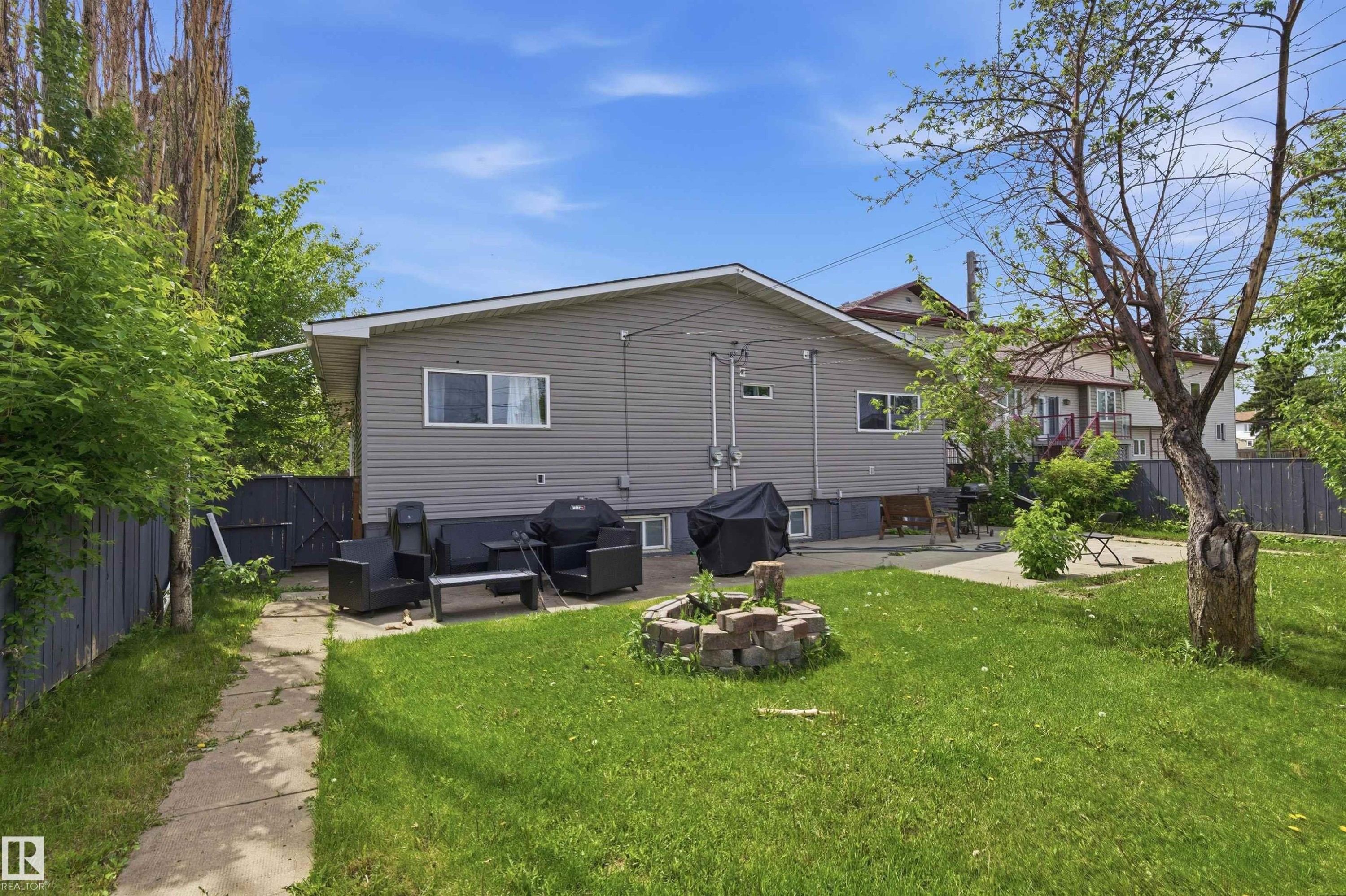 Expansive backyard featuring a manicured lawn, concrete patio, and mature trees - 7412/7414 83 Avenue Nw, Edmonton, AB - Outdoor