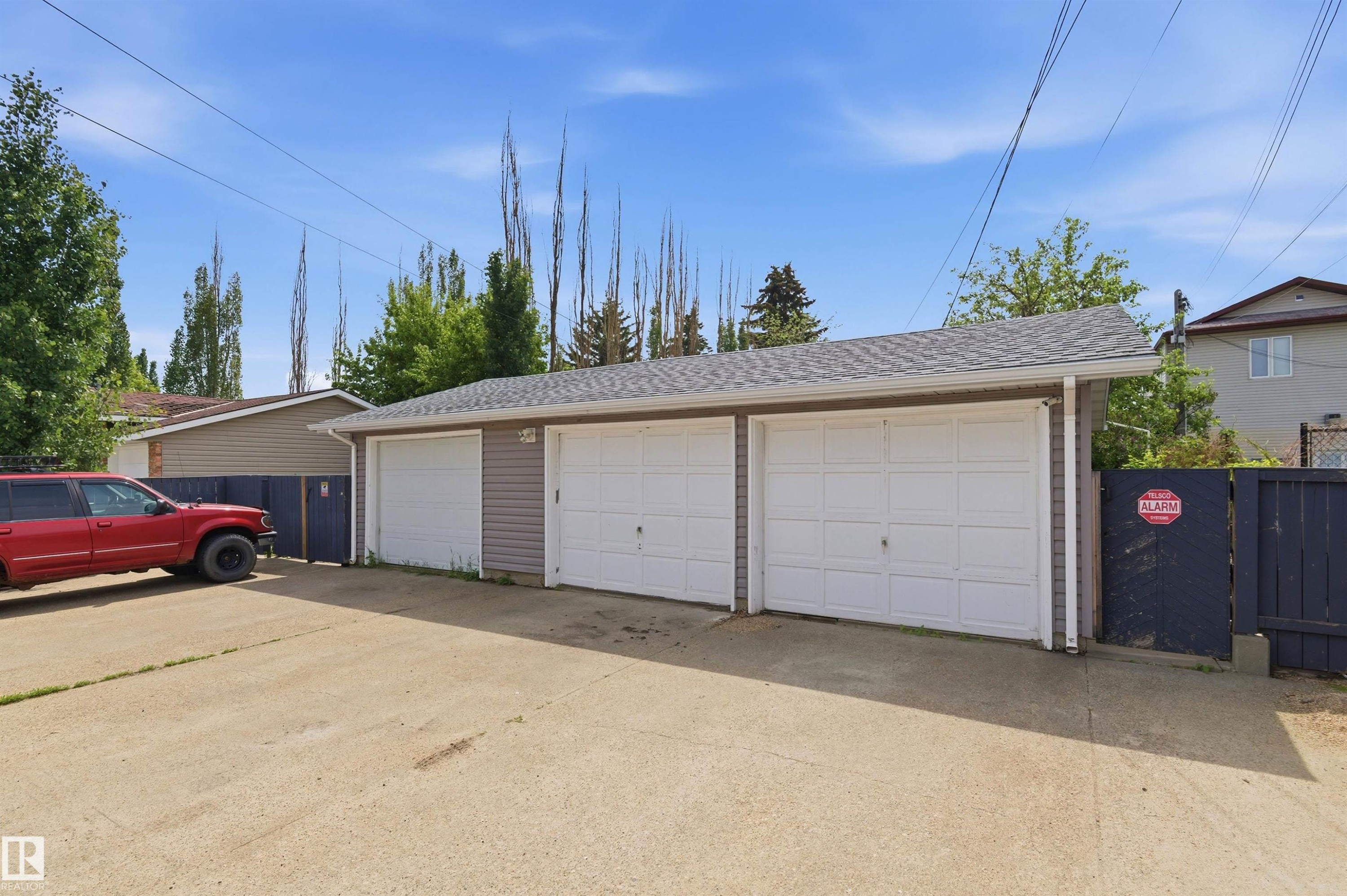 Triple-bay detached garage featuring light gray siding, white garage doors, and a shingled roof - 7412/7414 83 Avenue Nw, Edmonton, AB - Outdoor With Exterior