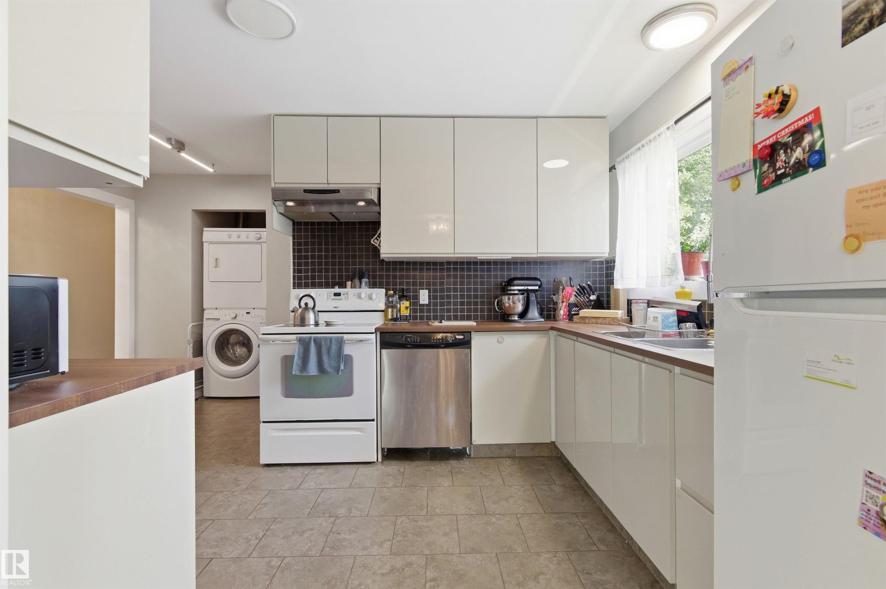 Kitchen featuring white flat-panel cabinetry, wood-finish countertops, tile flooring, and a dark tile backsplash - 7412/7414 83 Avenue Nw, Edmonton, AB - Indoor Photo Showing Kitchen