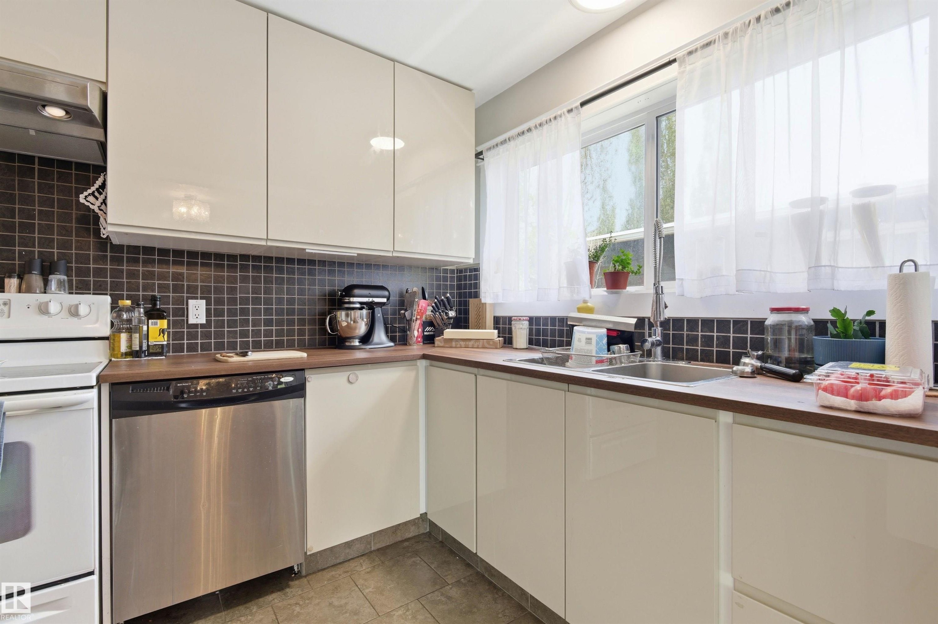 Kitchen featuring flat-panel cabinetry, a stainless steel dishwasher, wood-finish countertops, and a tile backsplash - 7412/7414 83 Avenue Nw, Edmonton, AB - Indoor Photo Showing Kitchen