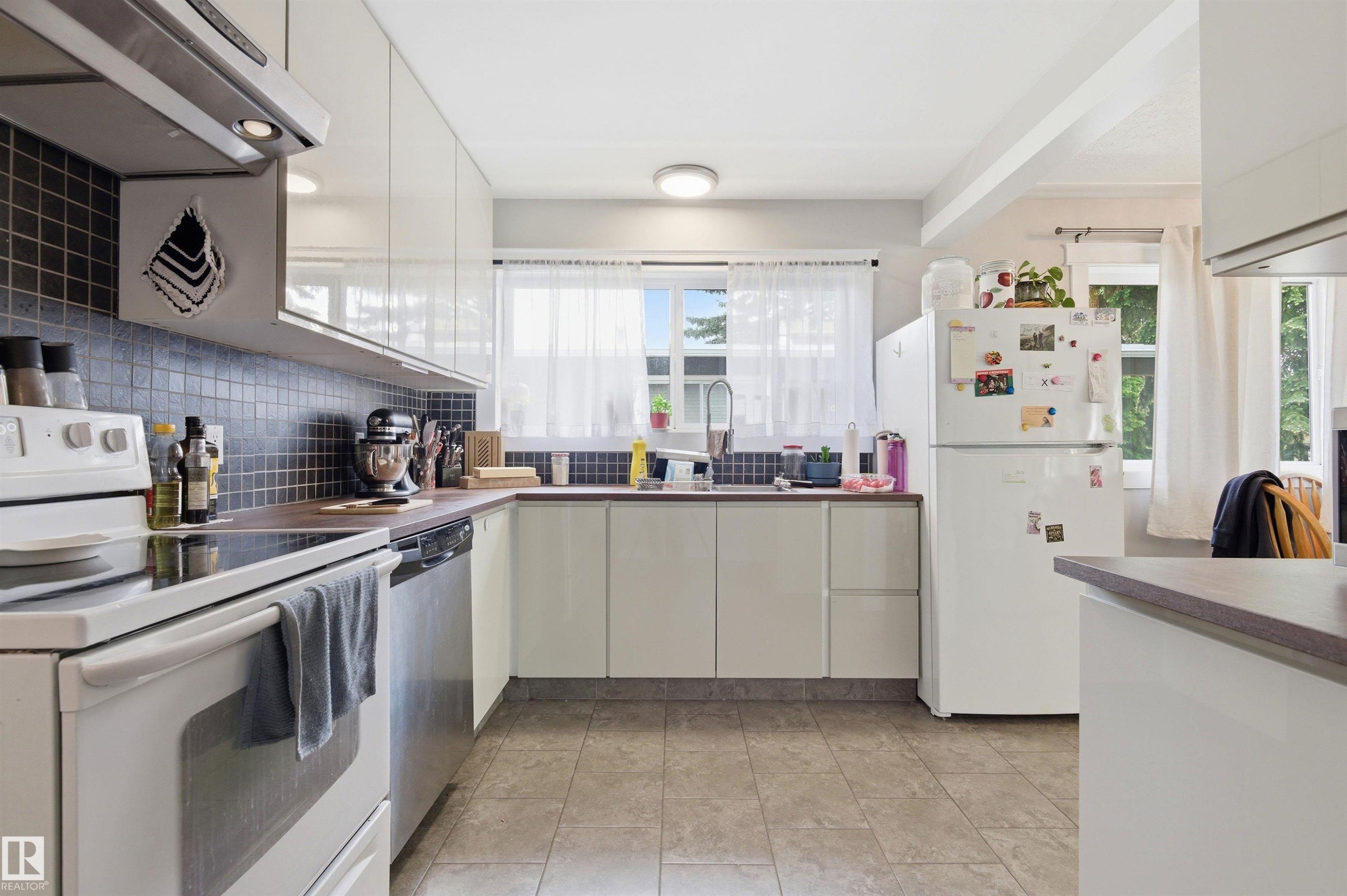 Bright kitchen with white cabinetry, stainless steel dishwasher, and a white oven range - 7412/7414 83 Avenue Nw, Edmonton, AB - Indoor Photo Showing Kitchen