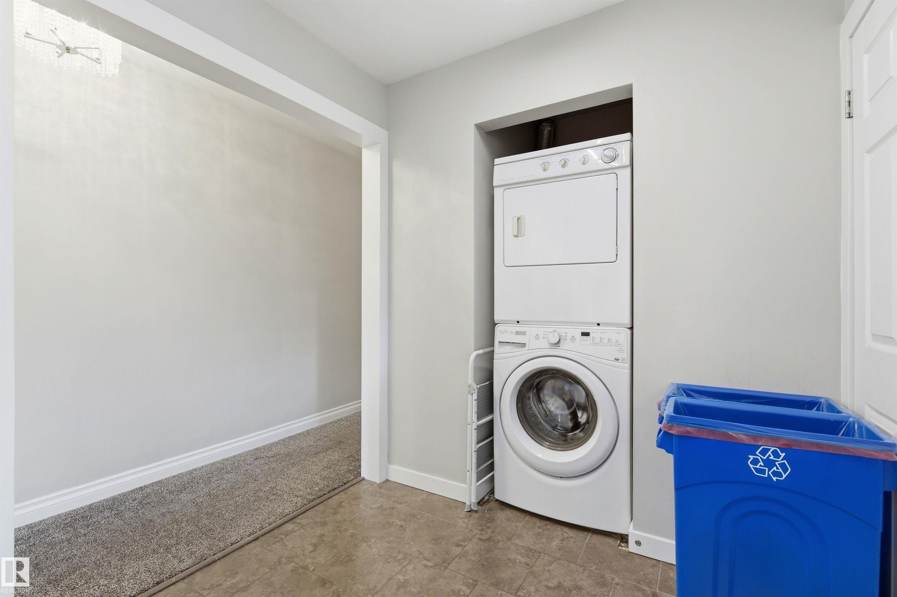 Dedicated laundry alcove featuring a stacked washer and dryer unit, complemented by neutral tile flooring - 7412/7414 83 Avenue Nw, Edmonton, AB - Indoor Photo Showing Laundry Room