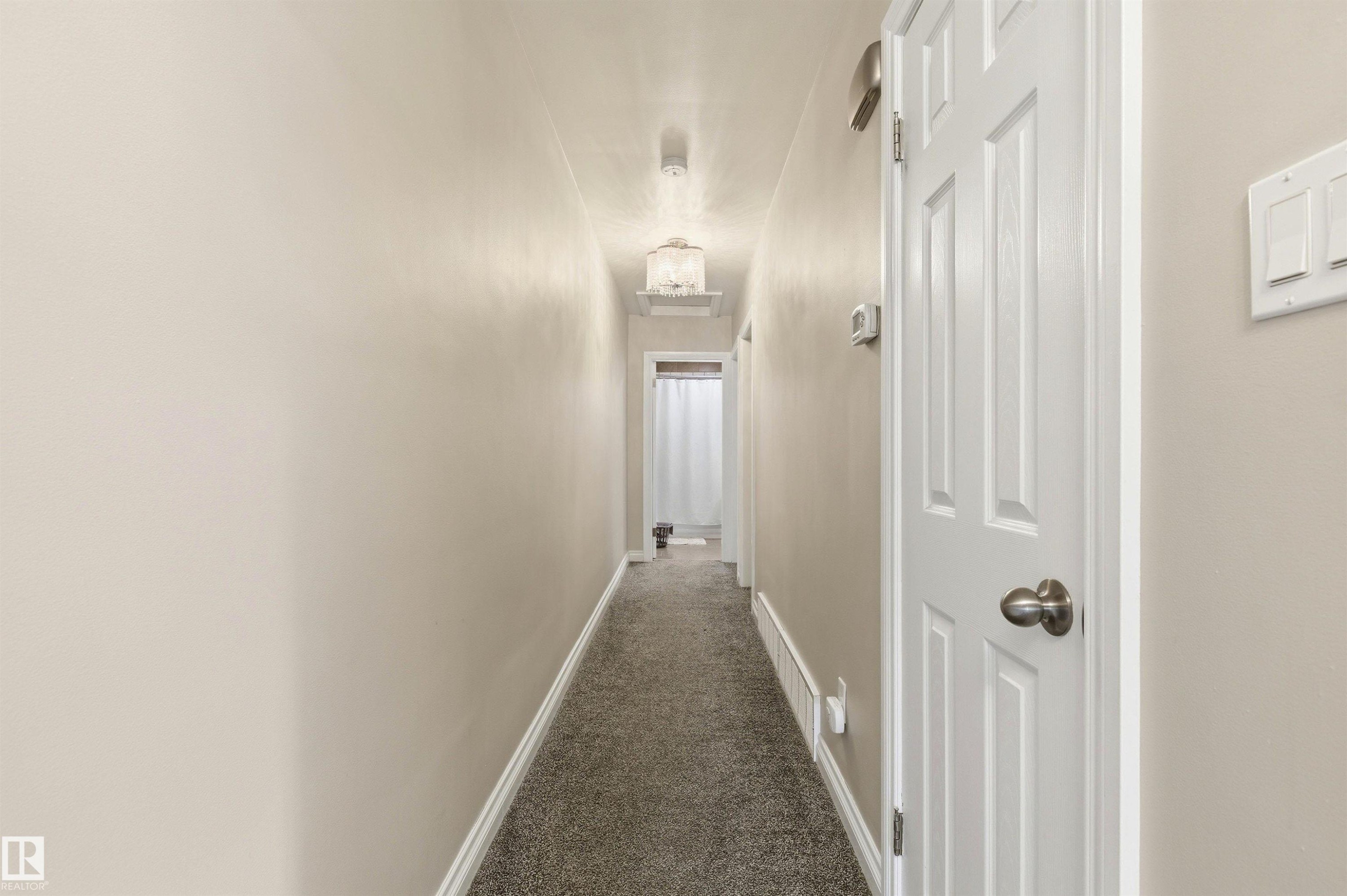 Carpeted hallway with light neutral wall paint and white baseboards - 7412/7414 83 Avenue Nw, Edmonton, AB - Indoor Photo Showing Other Room