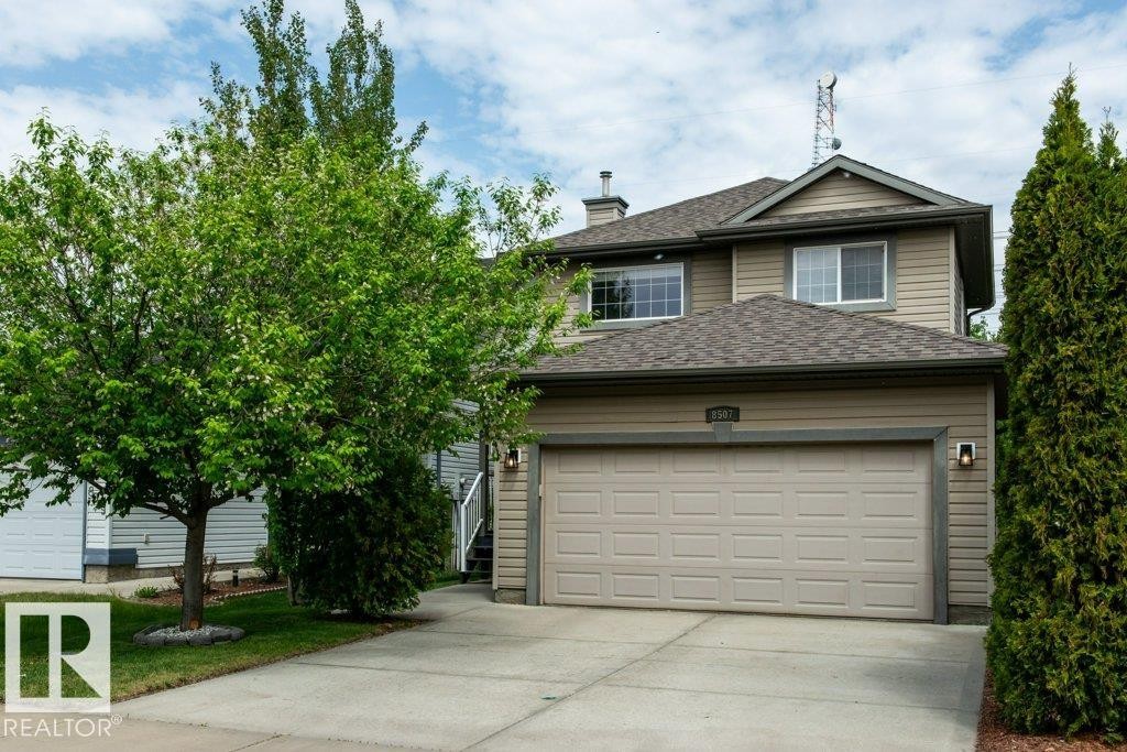 Exterior featuring beige horizontal siding, a two-car garage, concrete driveway, and mature landscaping - 8507 2 Avenue Sw, Edmonton, AB - Outdoor