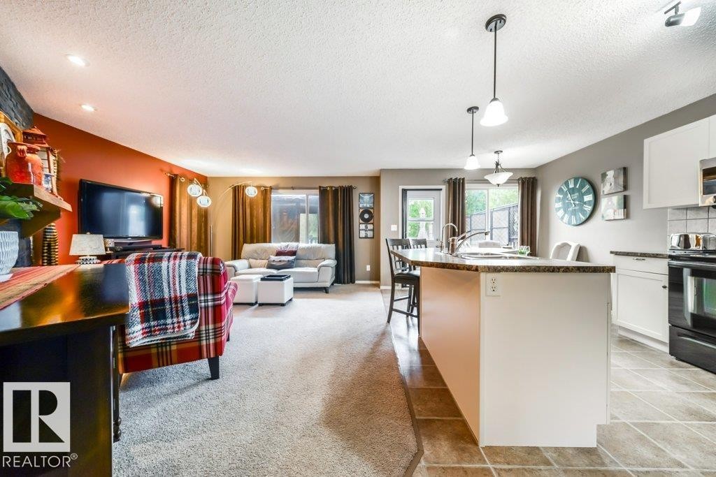 Open-concept living space featuring a kitchen island with seating, pendant lighting, stainless-steel sink, and a glass-paneled door leading to an exterior area - 8507 2 Avenue Sw, Edmonton, AB - Indoor Photo Showing Kitchen