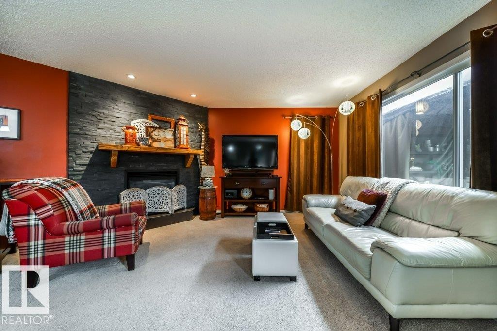 Living area featuring a textured stone-finish fireplace surround with a wood mantel, soft carpeting, recessed lighting, and a sliding glass door - 8507 2 Avenue Sw, Edmonton, AB - Indoor Photo Showing Living Room With Fireplace