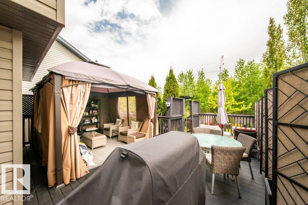 Expansive dark-toned deck featuring a covered gazebo with privacy curtains, a decorative privacy screen, and a glass-top dining table - 8507 2 Avenue Sw, Edmonton, AB - Outdoor With Deck Patio Veranda With Exterior