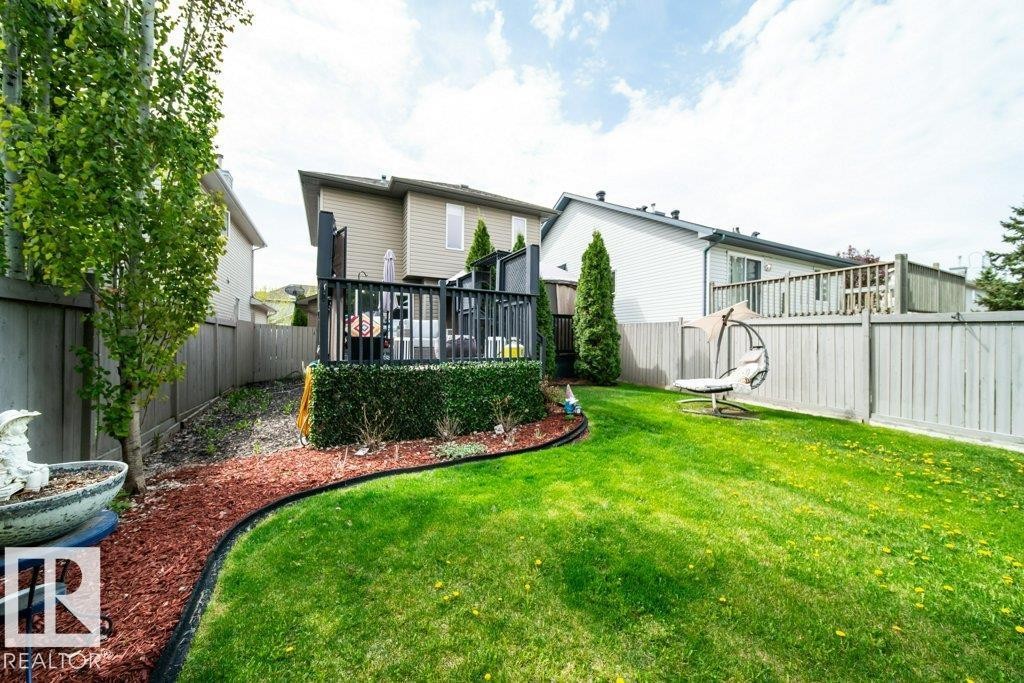 Landscaped backyard featuring a manicured lawn, a two-story deck with dark railings, a privacy fence, and mature trees - 8507 2 Avenue Sw, Edmonton, AB - Outdoor With Deck Patio Veranda