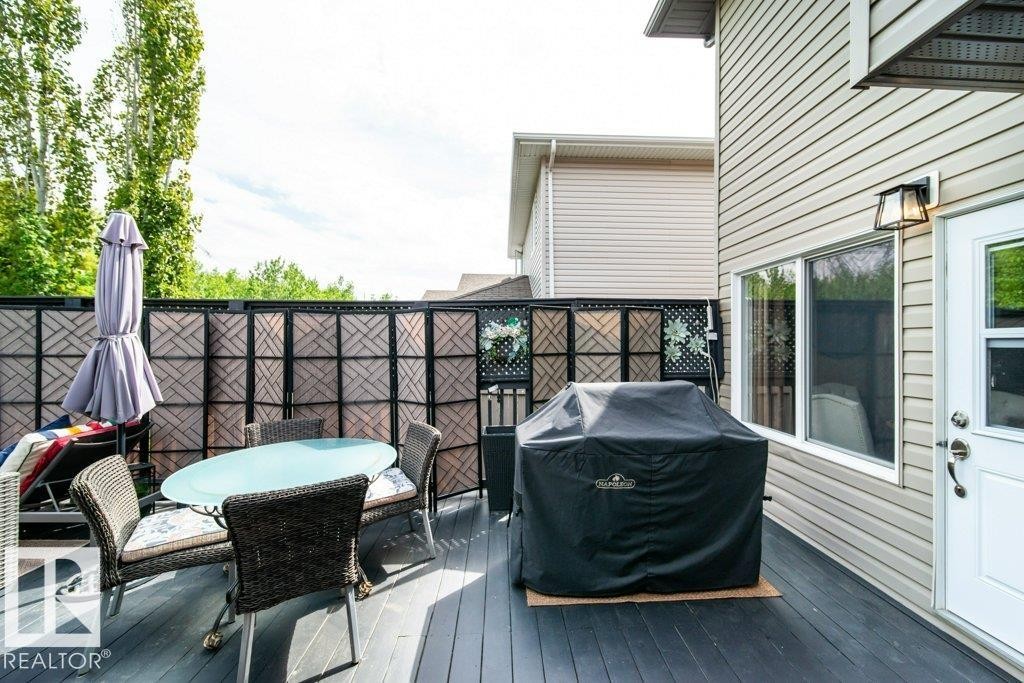 Spacious exterior deck with dark wood-finish flooring, featuring a decorative privacy screen, light-colored siding, and an exterior wall lantern - 8507 2 Avenue Sw, Edmonton, AB - Outdoor With Deck Patio Veranda With Exterior