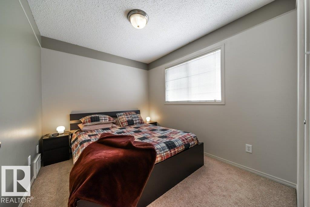 Neutral-toned bedroom featuring wall-to-wall carpeting, a horizontal window with blinds, and a built-in ceiling light fixture - 8507 2 Avenue Sw, Edmonton, AB - Indoor Photo Showing Bedroom
