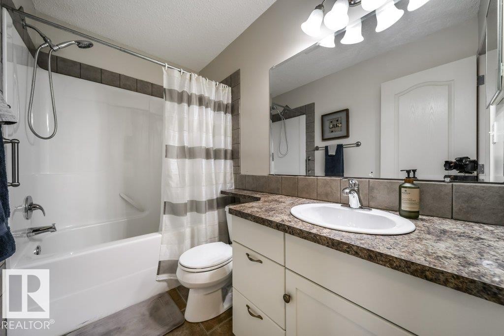 Bathroom featuring a white vanity with an undermount sink, a countertop with a stone-look finish, and a tile backsplash - 8507 2 Avenue Sw, Edmonton, AB - Indoor Photo Showing Bathroom