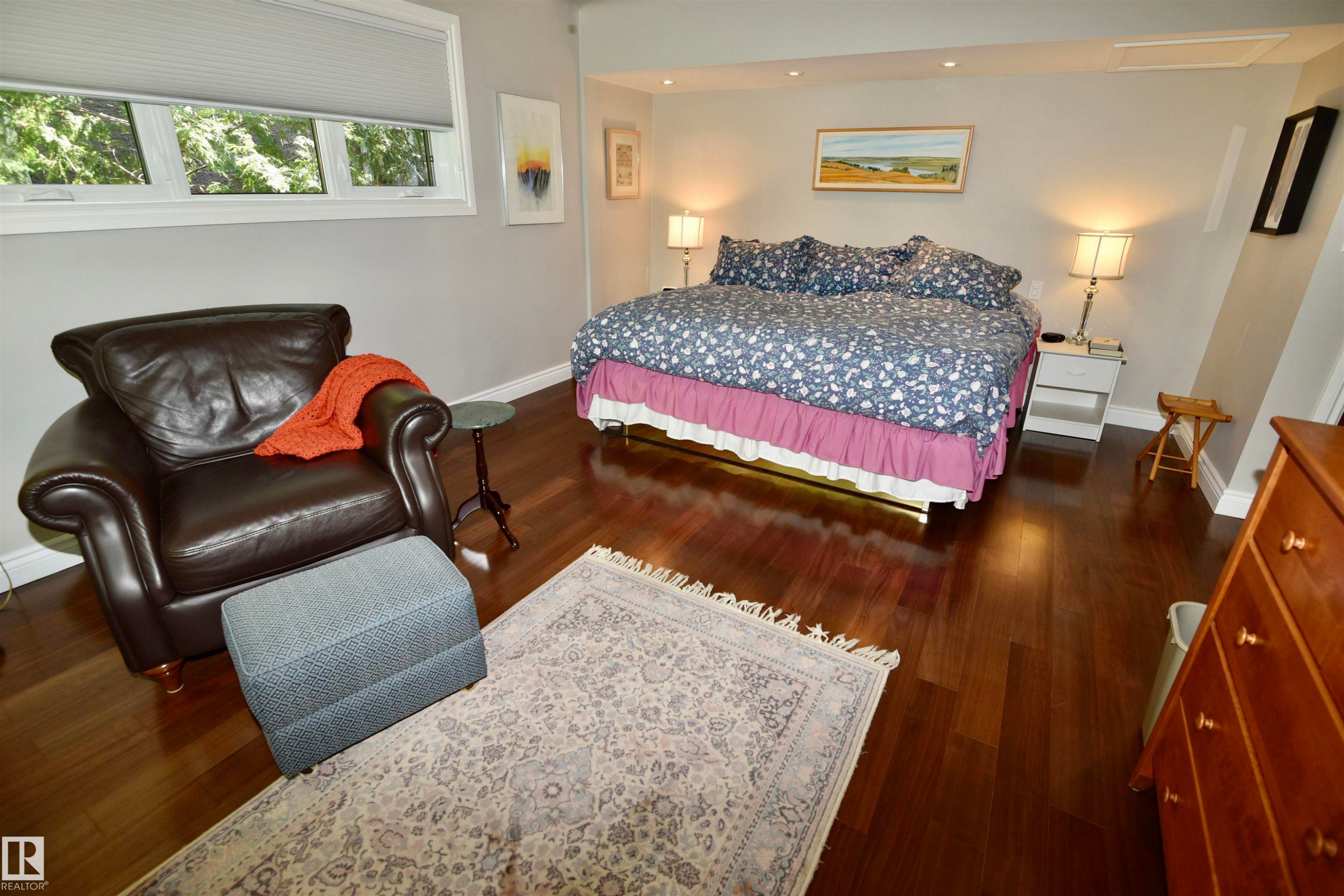 Spacious bedroom featuring rich wood-finish flooring, light grey wall tones, and recessed ceiling lighting - 6 St George'S Crescent, Edmonton, AB