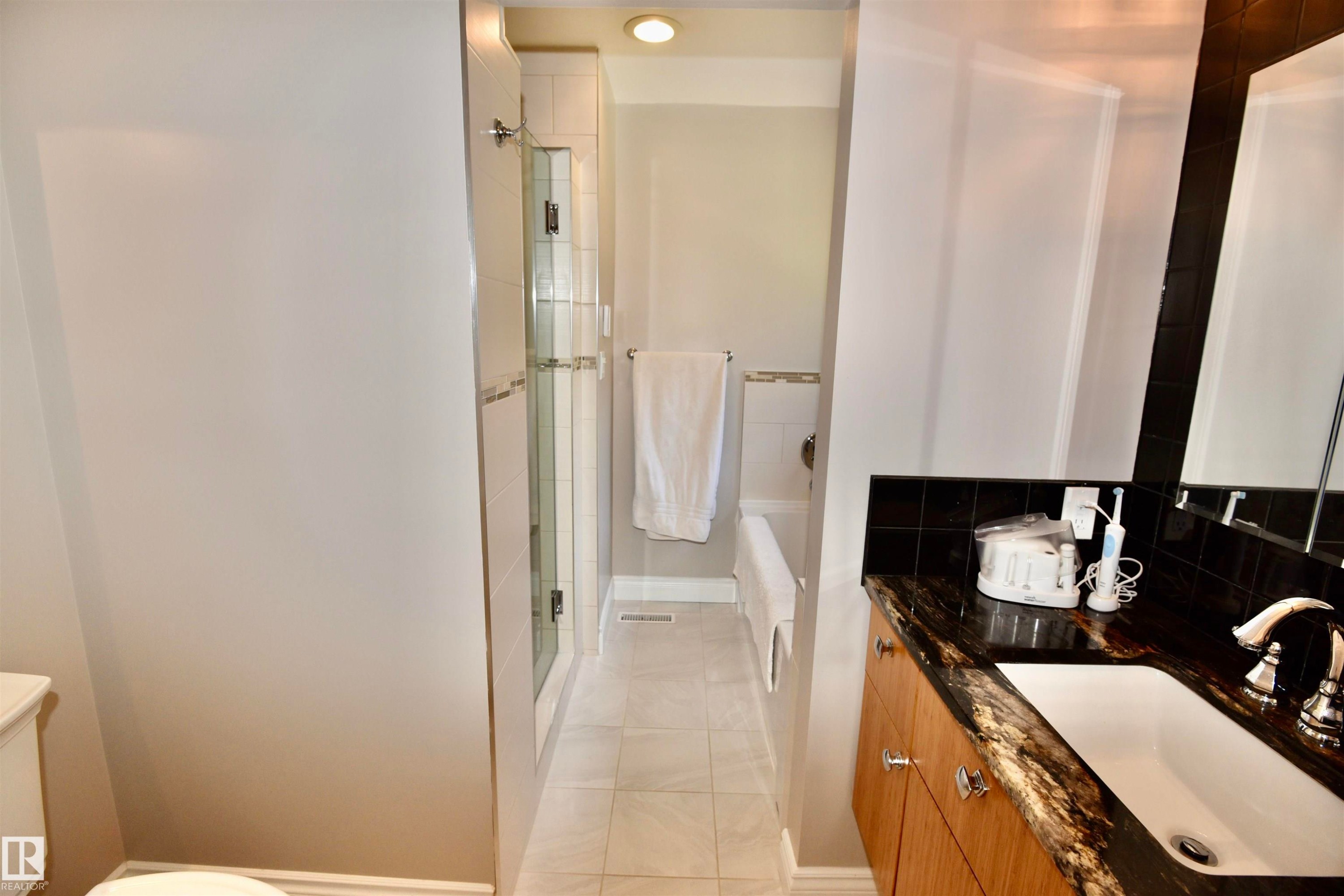 Bathroom featuring a dark stone countertop, wood-finish vanity with chrome hardware, an integrated sink, and a glass-enclosed shower - 6 St George'S Crescent, Edmonton, AB