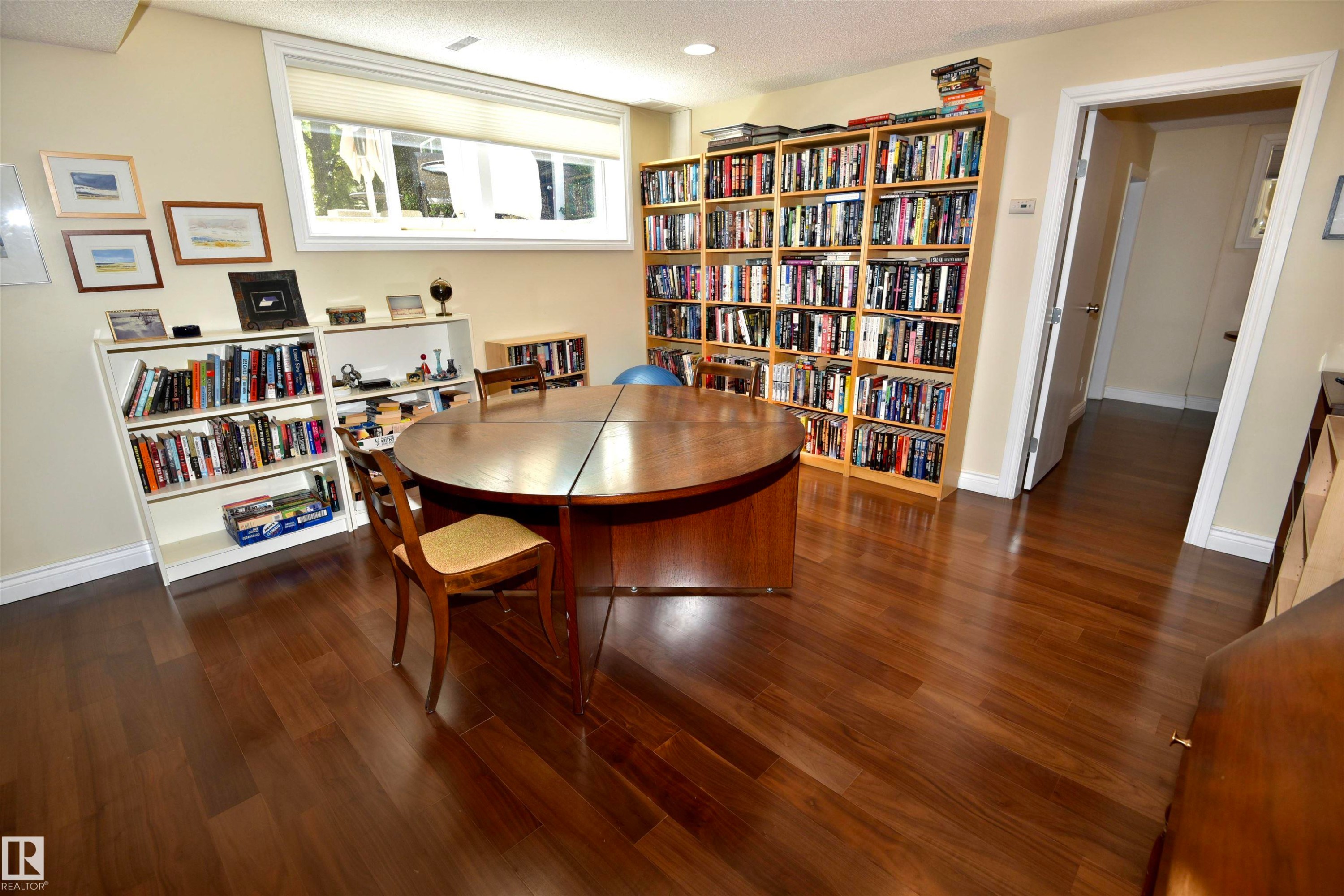 Expansive room featuring rich wood-finish flooring, a large wood folding table, a window with roller shades, and multiple built-in shelving units - 6 St George'S Crescent, Edmonton, AB