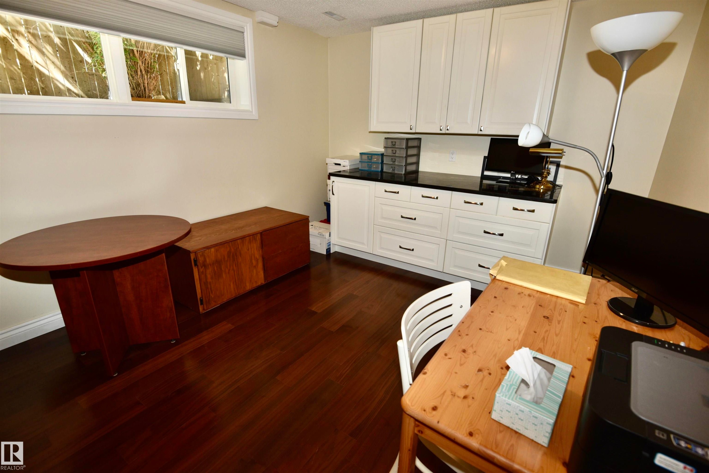 Cream cabinetry with black hardware, black countertop, wood-finish flooring, and a horizontal window with blinds - 6 St George'S Crescent, Edmonton, AB