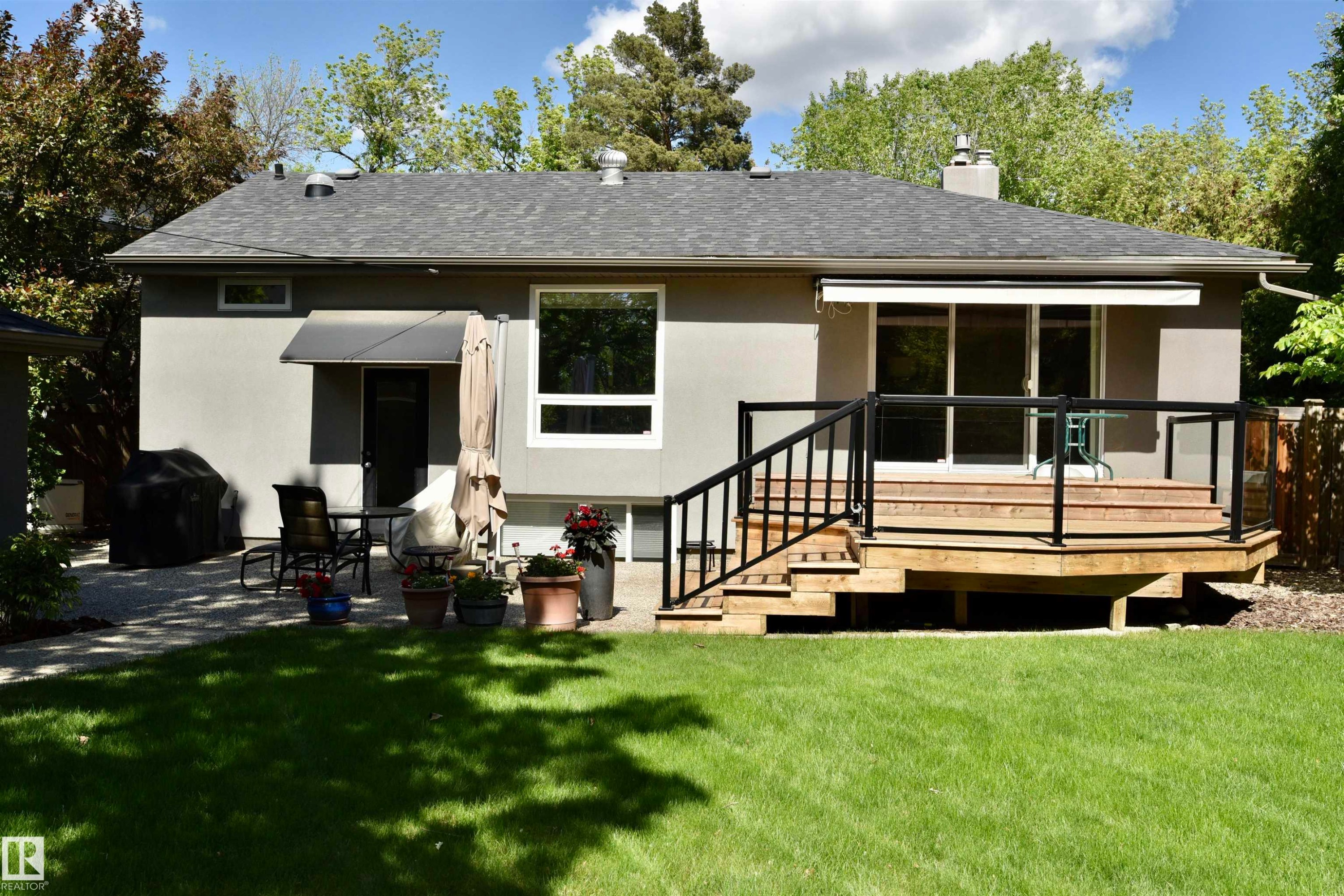 Expansive backyard featuring a manicured lawn, a multi-level wood deck with black railing and glass panels, and a concrete patio - 6 St George'S Crescent, Edmonton, AB