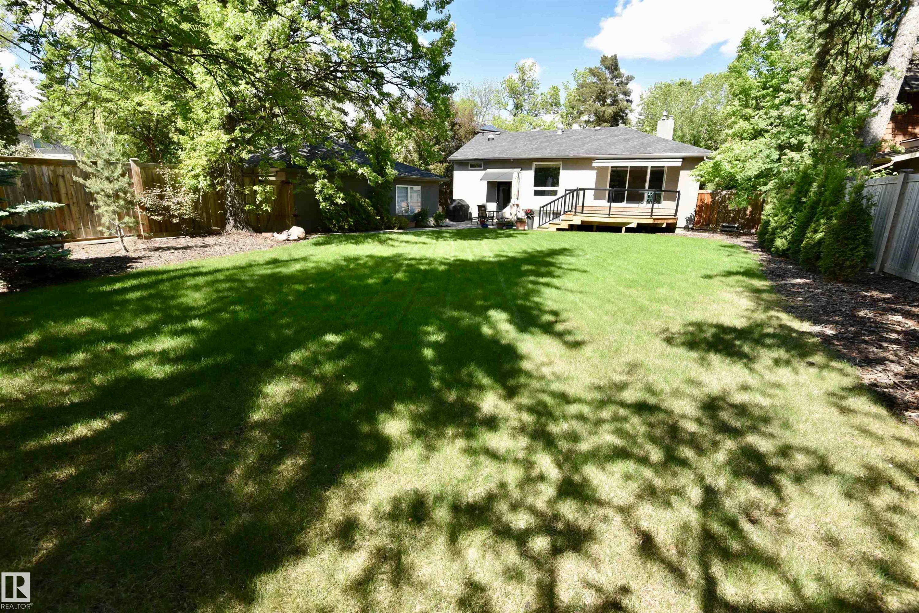 Expansive backyard featuring a manicured lawn, a raised wooden deck with dark railings, and mature perimeter trees - 6 St George'S Crescent, Edmonton, AB