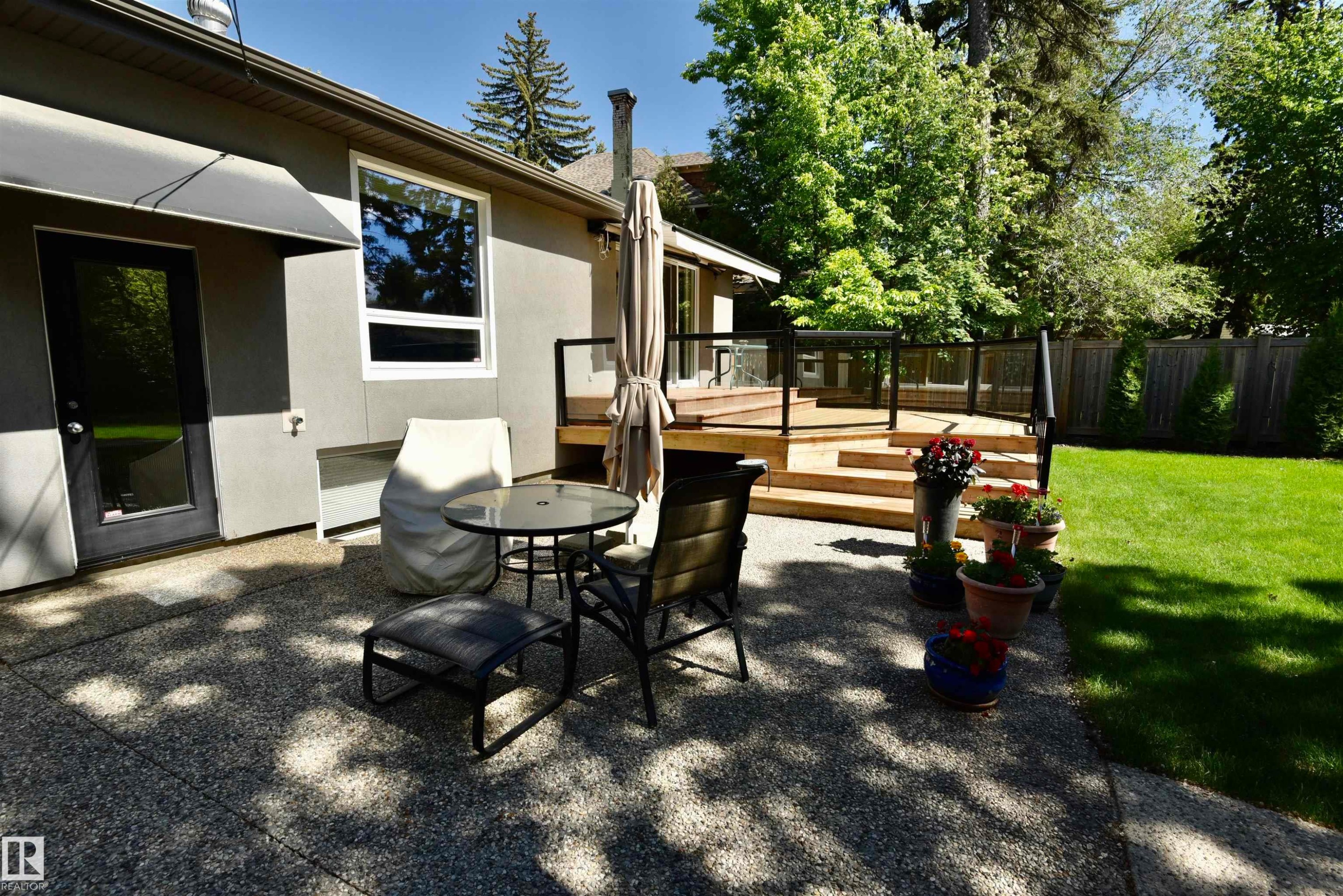 Expansive backyard featuring a multi-tiered wood deck with glass railing, a concrete patio area, and a manicured lawn - 6 St George'S Crescent, Edmonton, AB