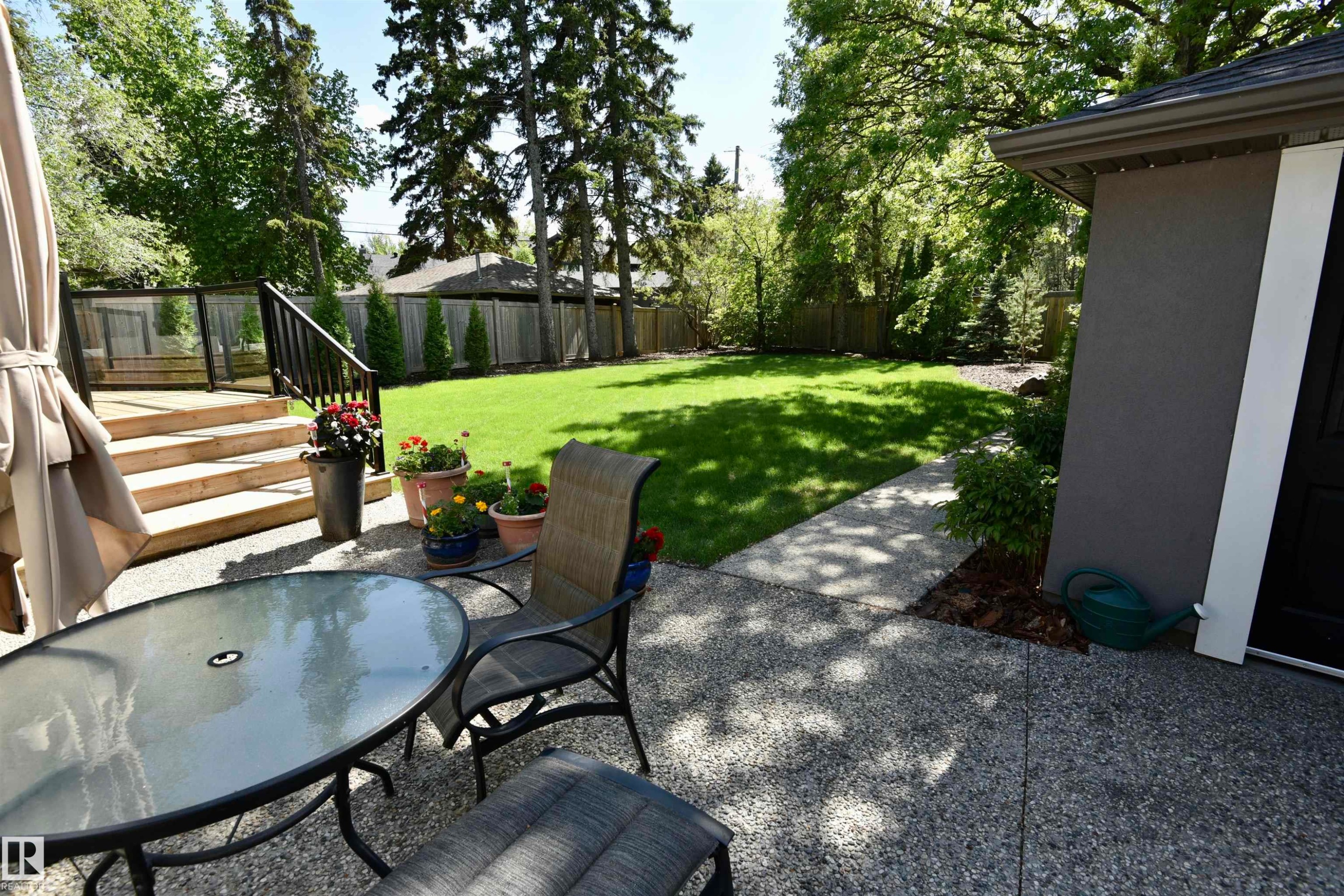 Expansive backyard featuring a manicured lawn, mature trees, and a wooden deck with black railings - 6 St George'S Crescent, Edmonton, AB