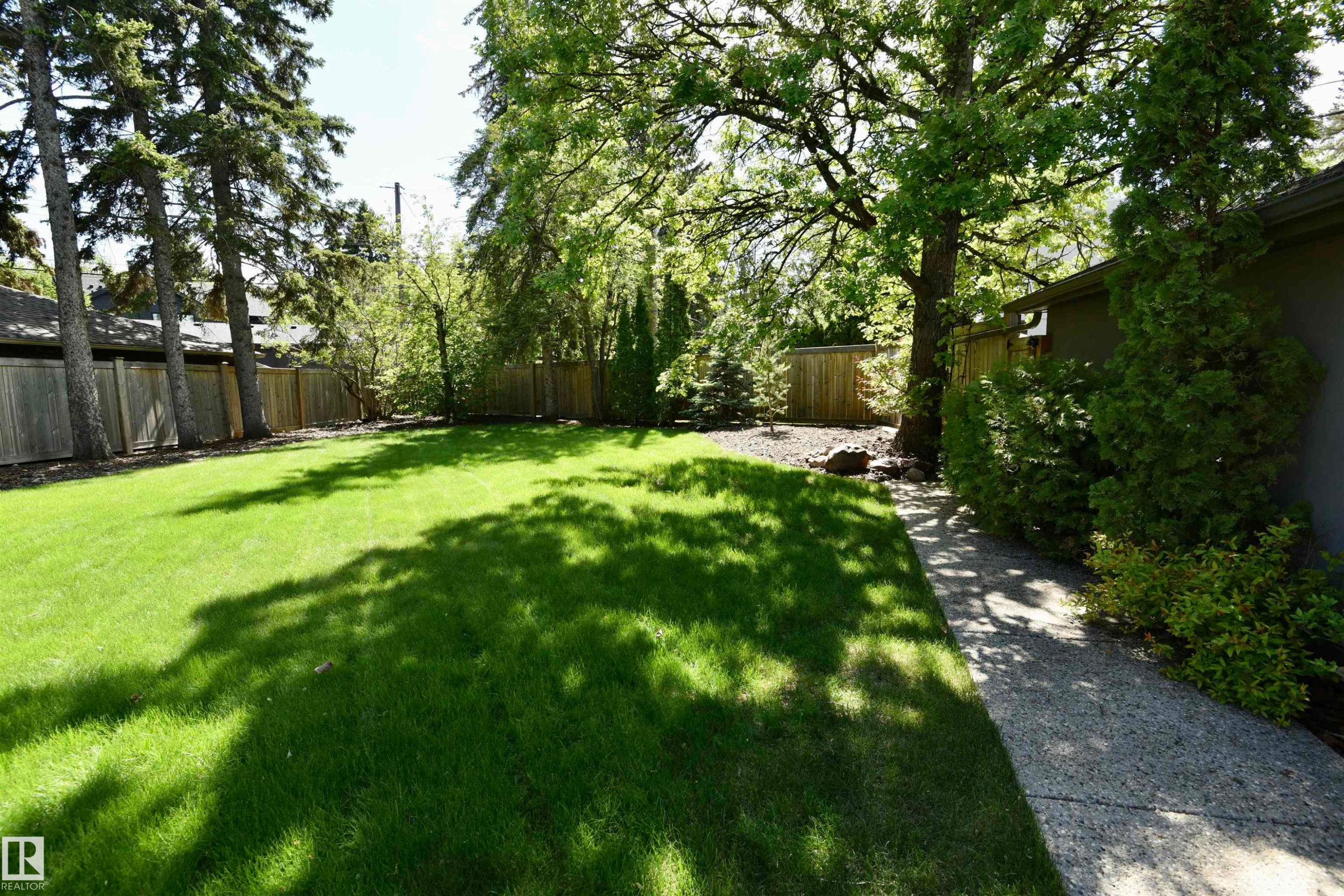 Expansive backyard featuring a manicured lawn, mature trees, a wood privacy fence, and a concrete pathway - 6 St George'S Crescent, Edmonton, AB
