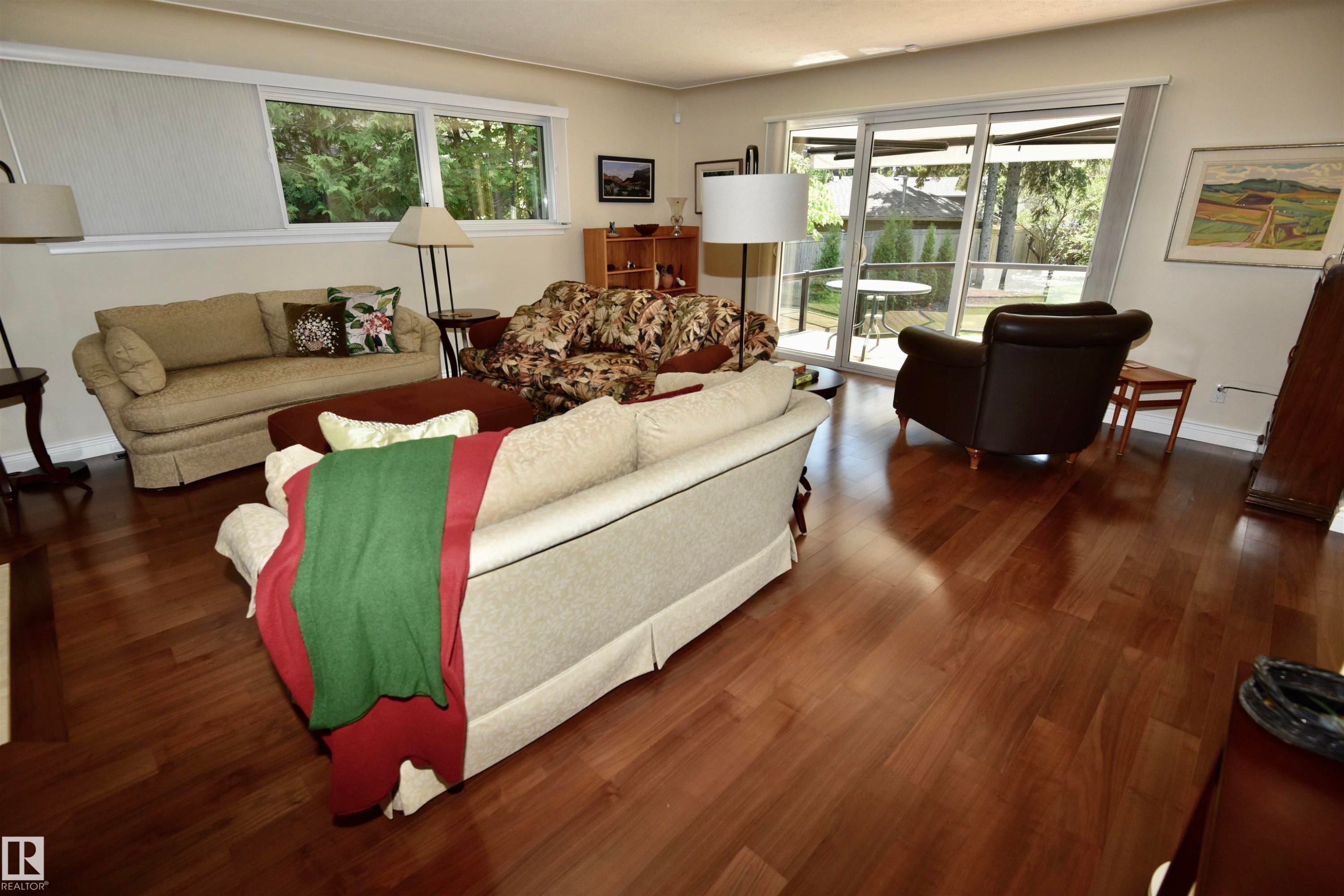Spacious living area featuring polished wood-finish flooring, white walls, and a multi-pane glass sliding door providing access to the exterior patio - 6 St George'S Crescent, Edmonton, AB