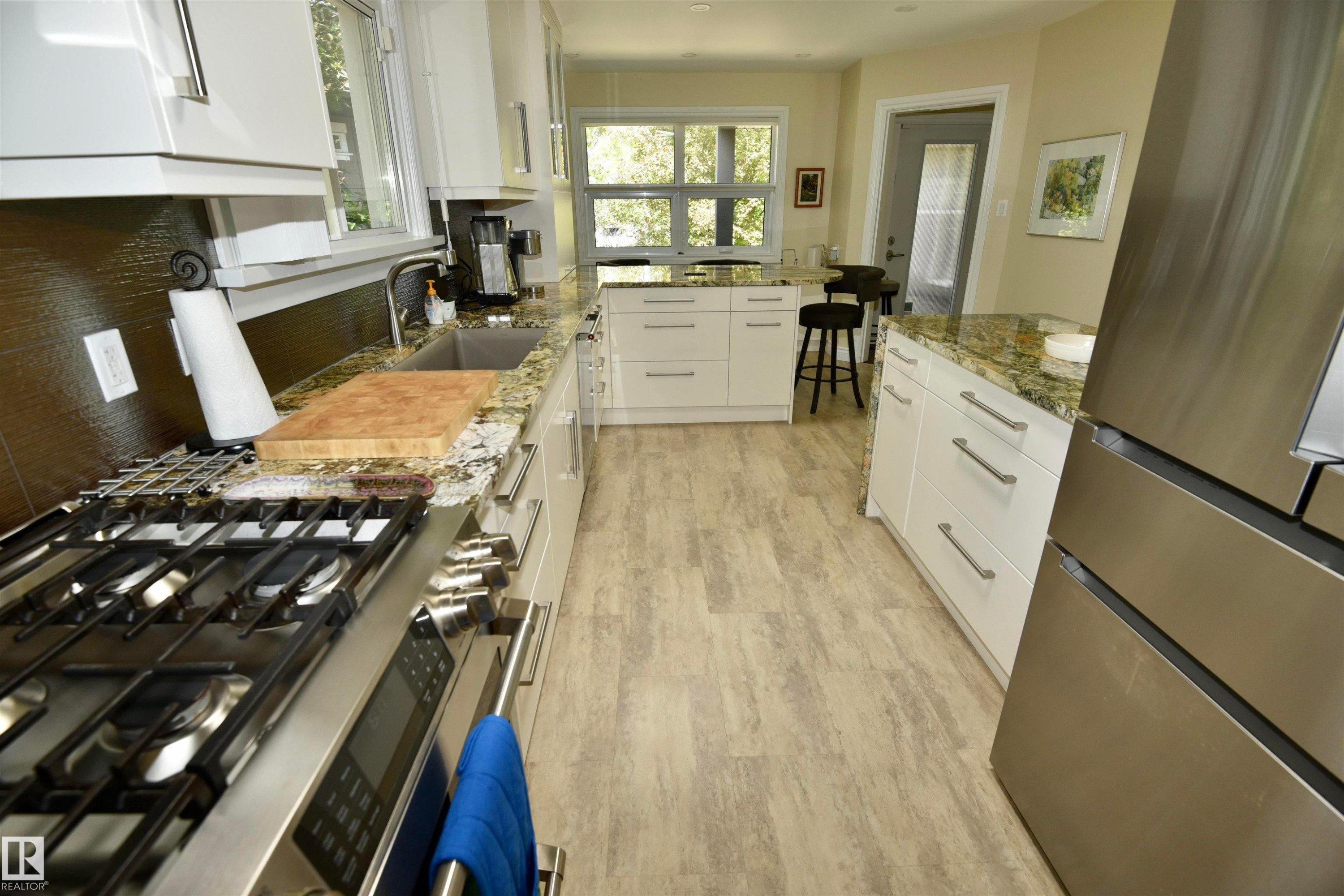 Contemporary kitchen featuring white cabinetry, stone countertops, stainless steel appliances, wood-finish flooring, and a central island with additional storage - 6 St George'S Crescent, Edmonton, AB