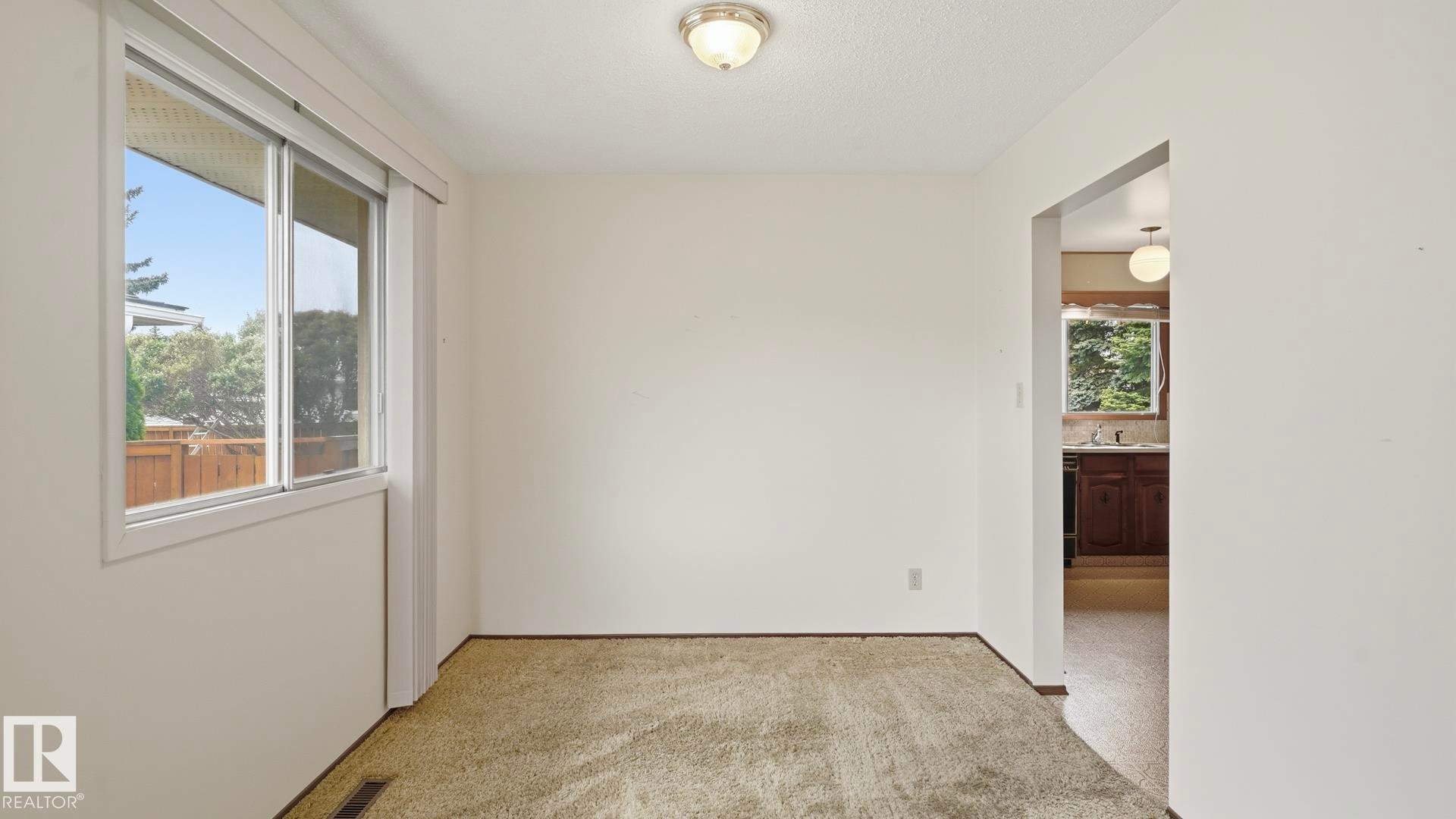 Carpeted room with a white ceiling and walls, featuring a window with white trim and an overhead flush-mount light fixture - 7408 40 Avenue, Edmonton, AB