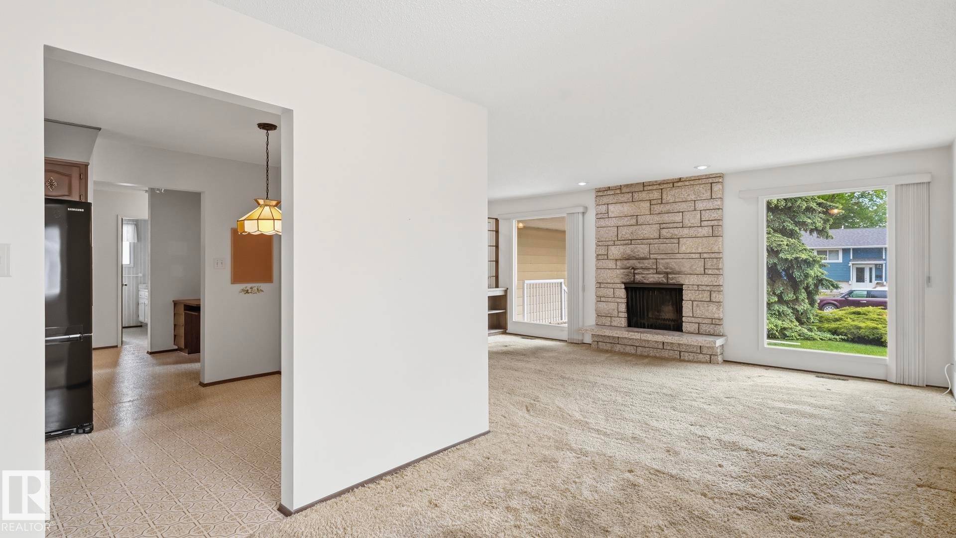 Living area featuring a stone-faced fireplace with a hearth, large windows, and recessed lighting - 7408 40 Avenue, Edmonton, AB