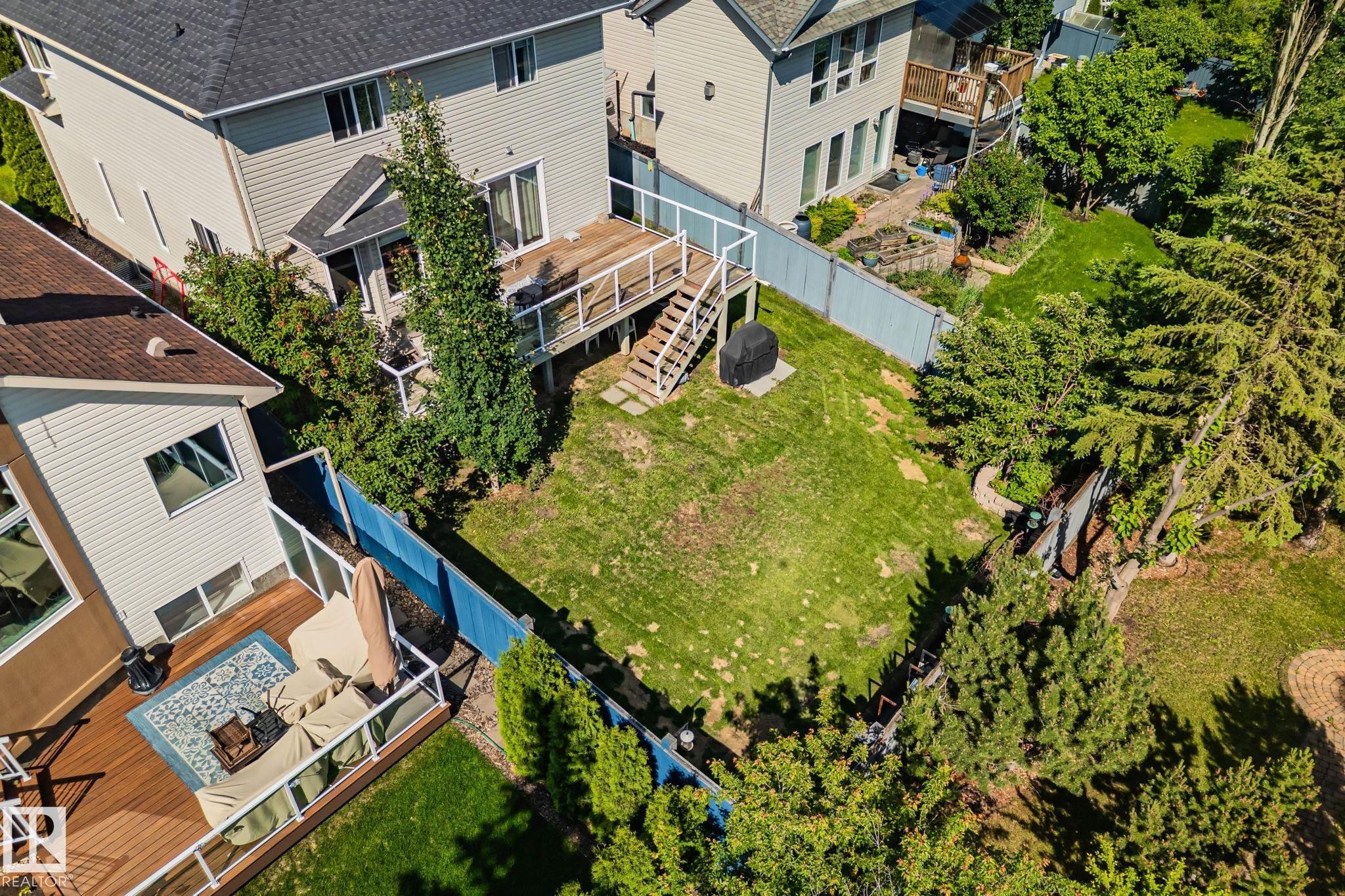 Expansive backyard featuring a manicured lawn, established landscaping, and a multi-level wooden deck with glass panel railings - 591 Byrne Crescent Sw, Edmonton, AB - Outdoor