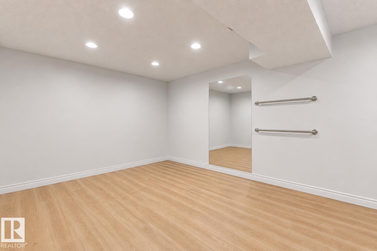 Bright interior space featuring wood-finish flooring, recessed lighting, a large wall-mounted mirror, and two parallel wall bars - 11234 40 Avenue Nw, Edmonton, AB - Indoor Photo Showing Other Room