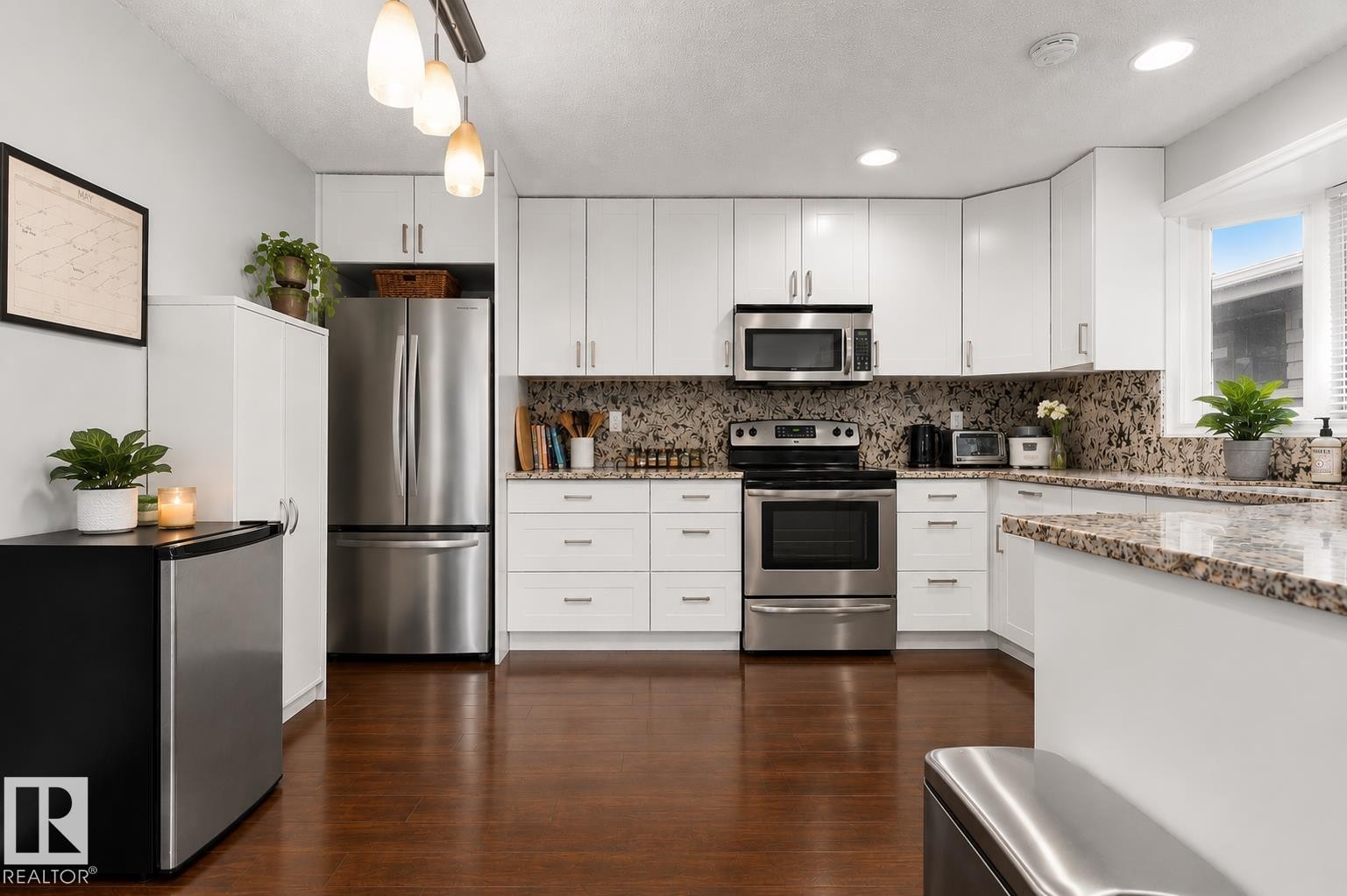 Modern kitchen featuring white cabinetry, stainless steel appliances, speckled stone countertops, a coordinating stone backsplash, and wood-finish flooring - 11234 40 Avenue Nw, Edmonton, AB - Indoor Photo Showing Kitchen With Stainless Steel Kitchen With Upgraded Kitchen