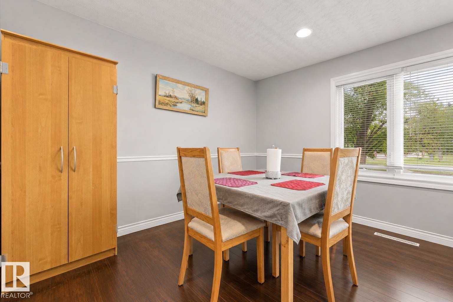 Dining area featuring dark wood-finish flooring, light grey walls with white chair rail molding, and a large window providing natural light - 11234 40 Avenue Nw, Edmonton, AB - Indoor Photo Showing Dining Room