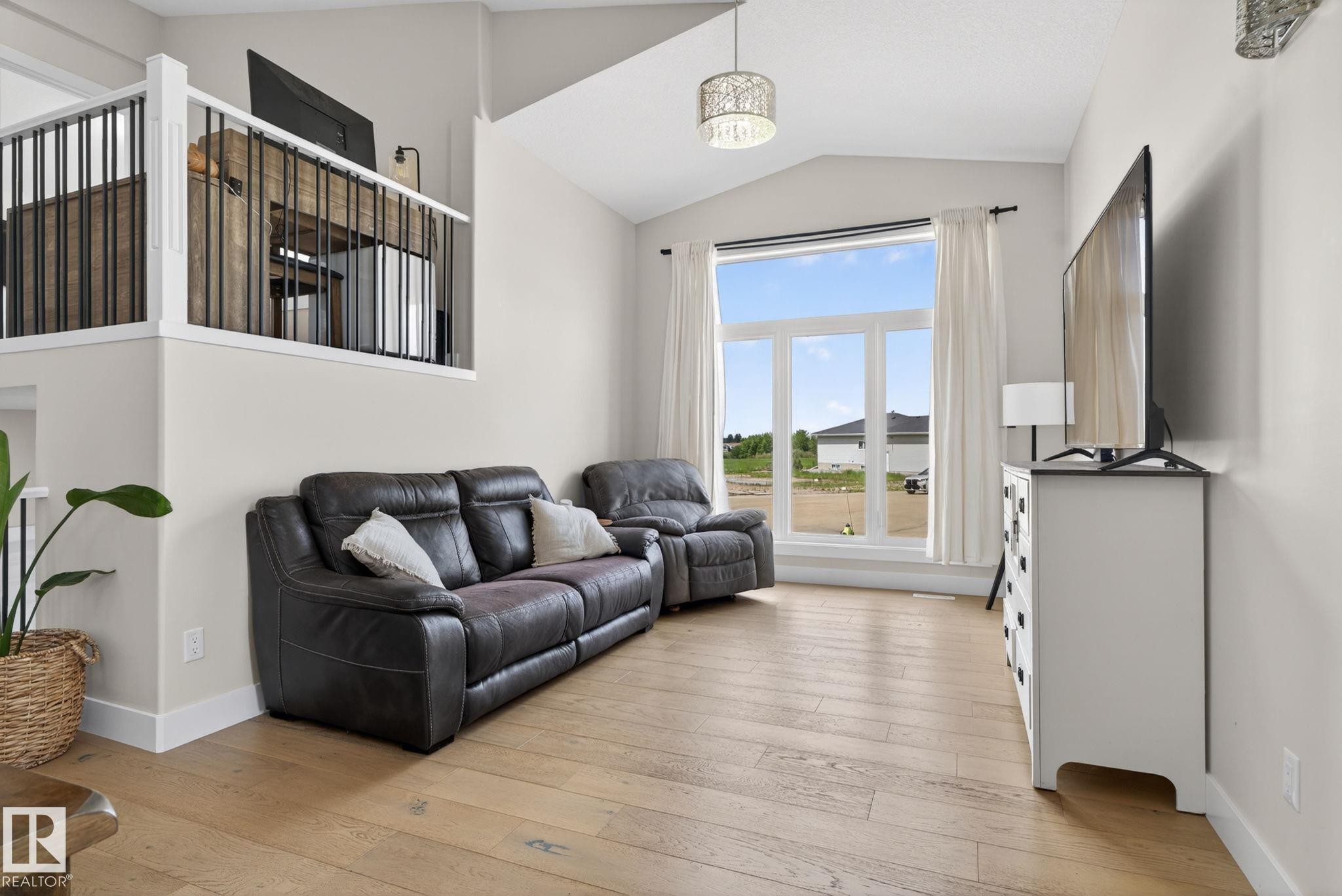 Living area featuring wood-finish flooring, a contemporary chandelier, and a large window - 4204 55Av, Lamont, AB