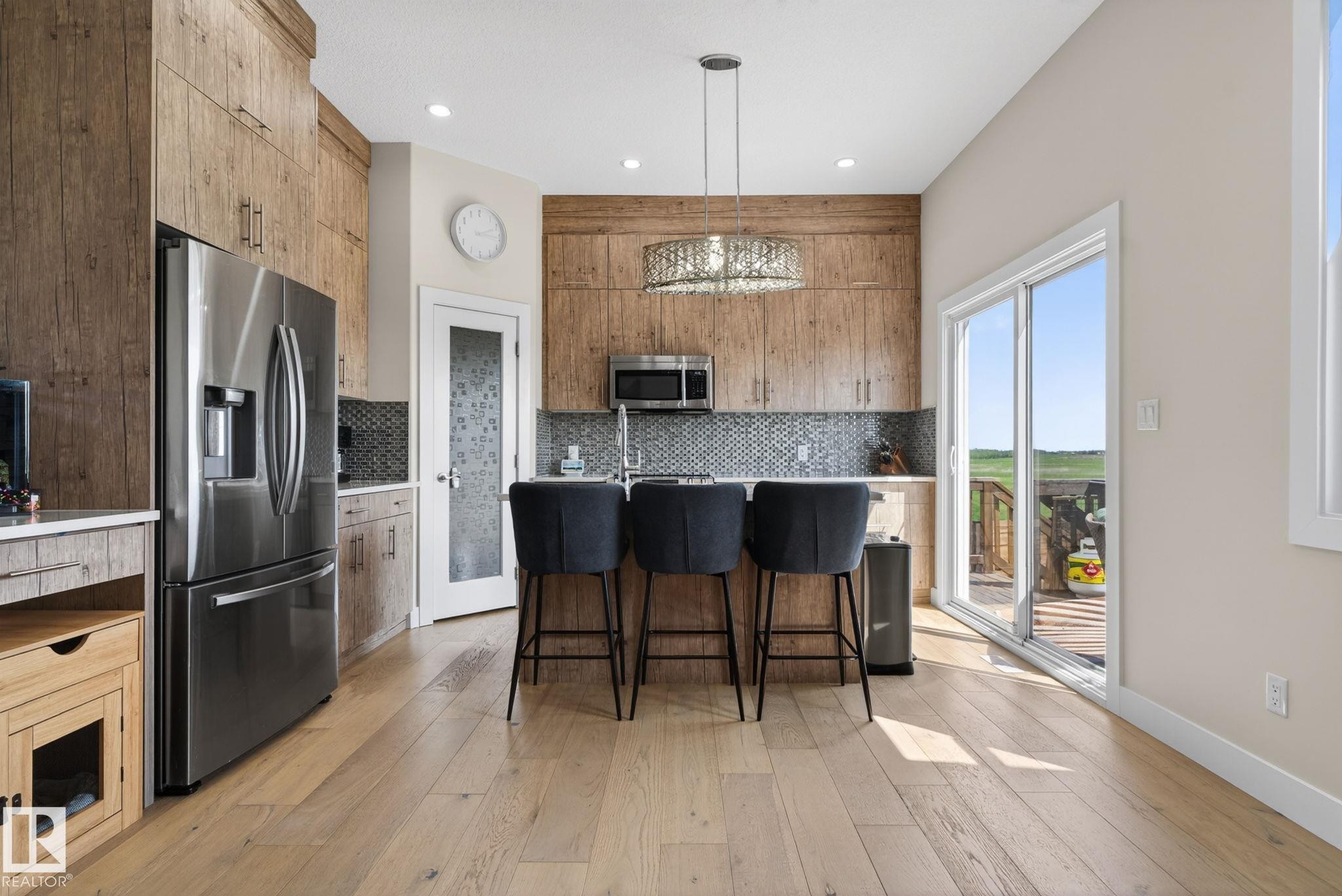 Kitchen featuring wood-finish cabinetry, stainless steel appliances, a mosaic tile backsplash, a central island with bar seating, and wood-finish flooring - 4204 55Av, Lamont, AB