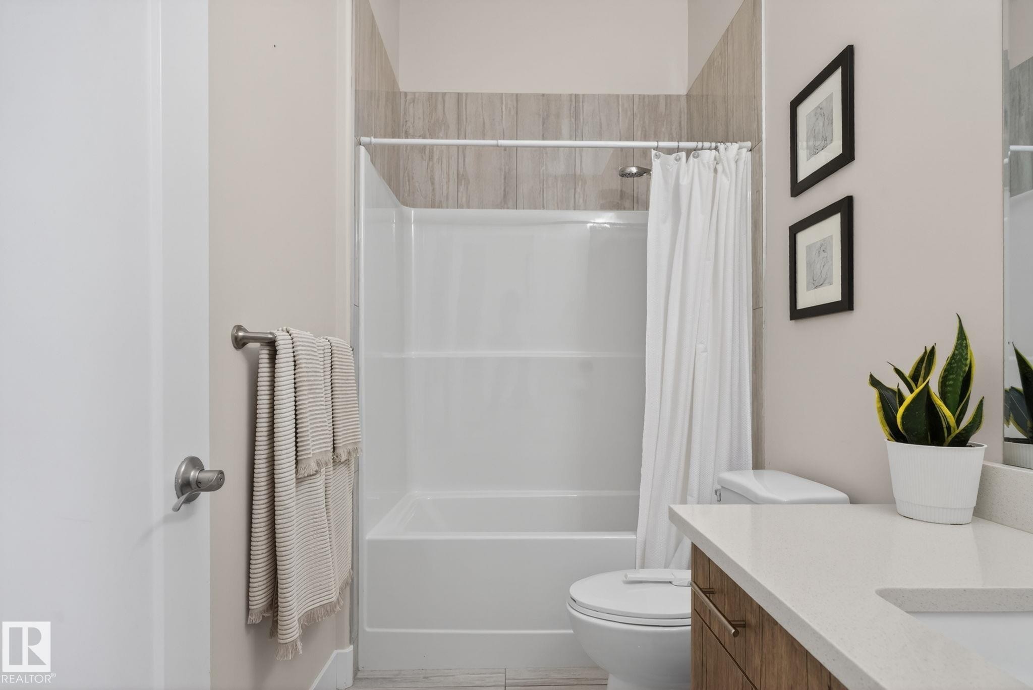Bathroom featuring a white shower/tub combination with tiled surround, a toilet, and a vanity with a light-toned countertop - 4204 55Av, Lamont, AB