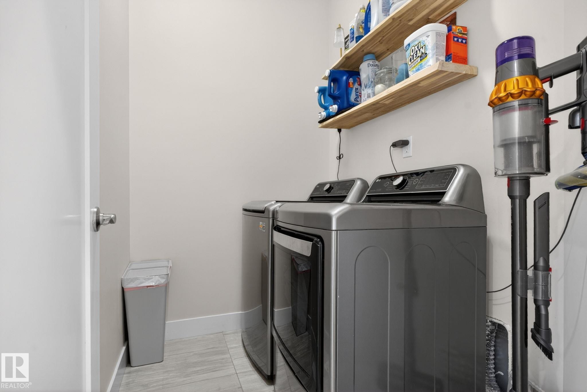 Laundry area featuring contemporary gray appliances, open wood shelving, and light wall tones - 4204 55Av, Lamont, AB