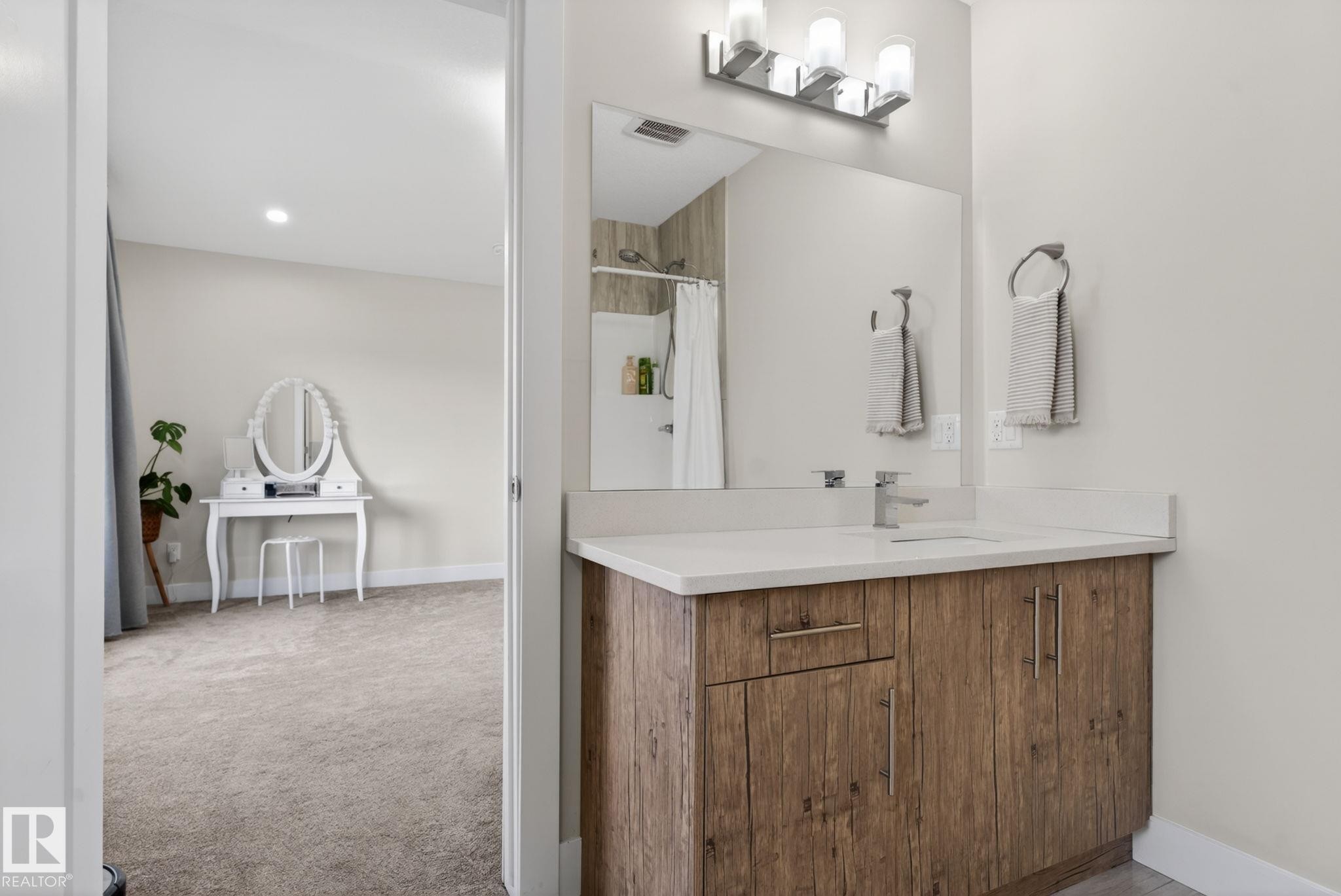 Bathroom featuring a wood-finish vanity with a light-toned countertop, a rectangular undermount sink, and a large wall-mounted mirror - 4204 55Av, Lamont, AB