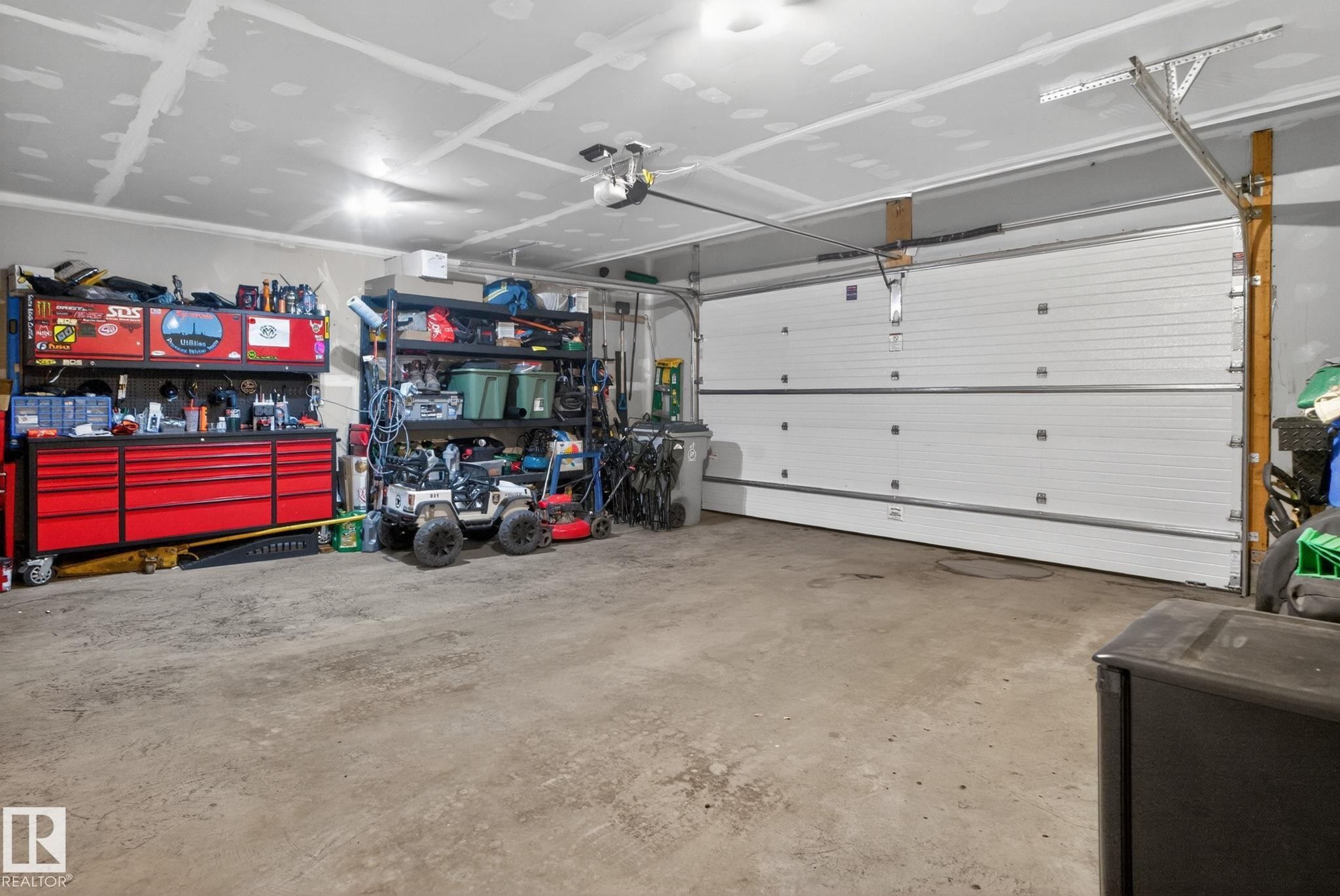Spacious garage with a concrete floor, white panel garage door, and ample overhead lighting - 4204 55Av, Lamont, AB